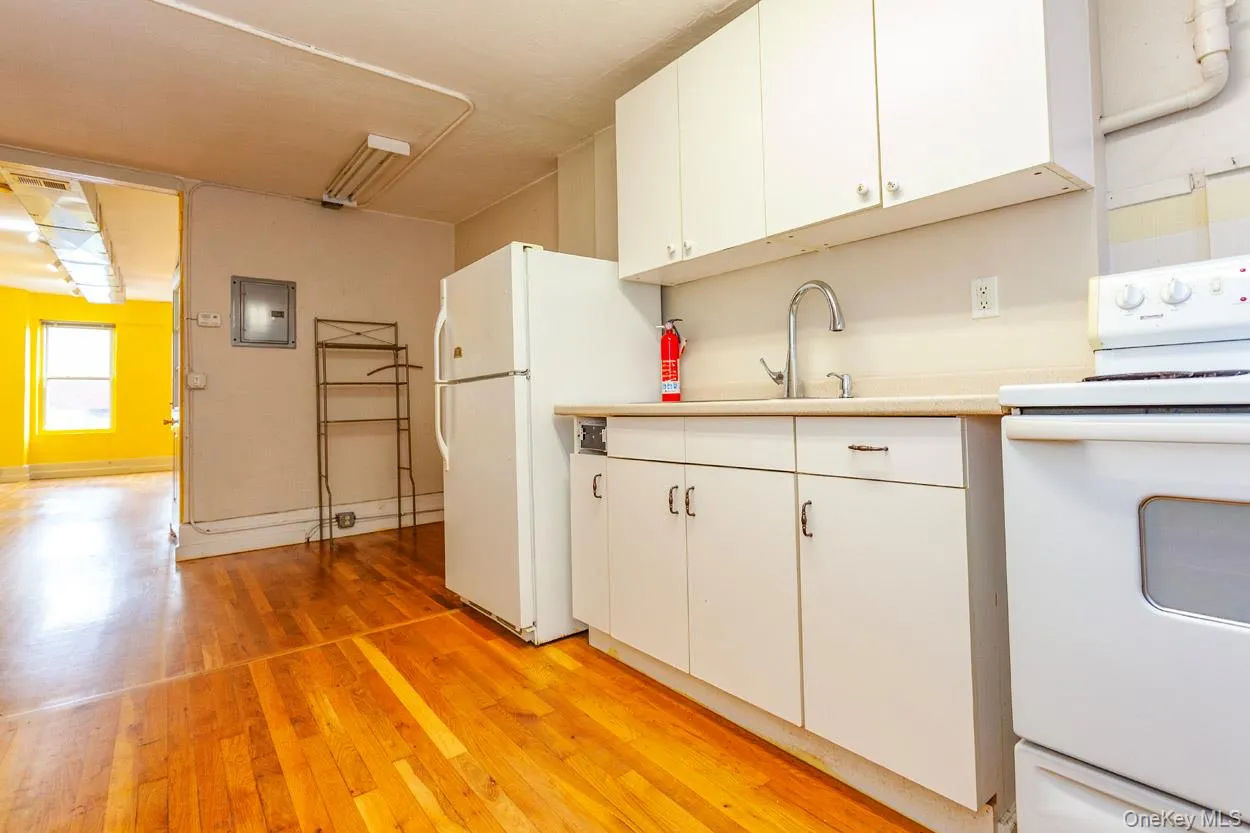 Kitchen with white appliances, light wood finished floors, light countertops, white cabinetry, and electric panel Kitchen with white appliances, light wood finished floors, light countertops, white cabinetry, and electric panel