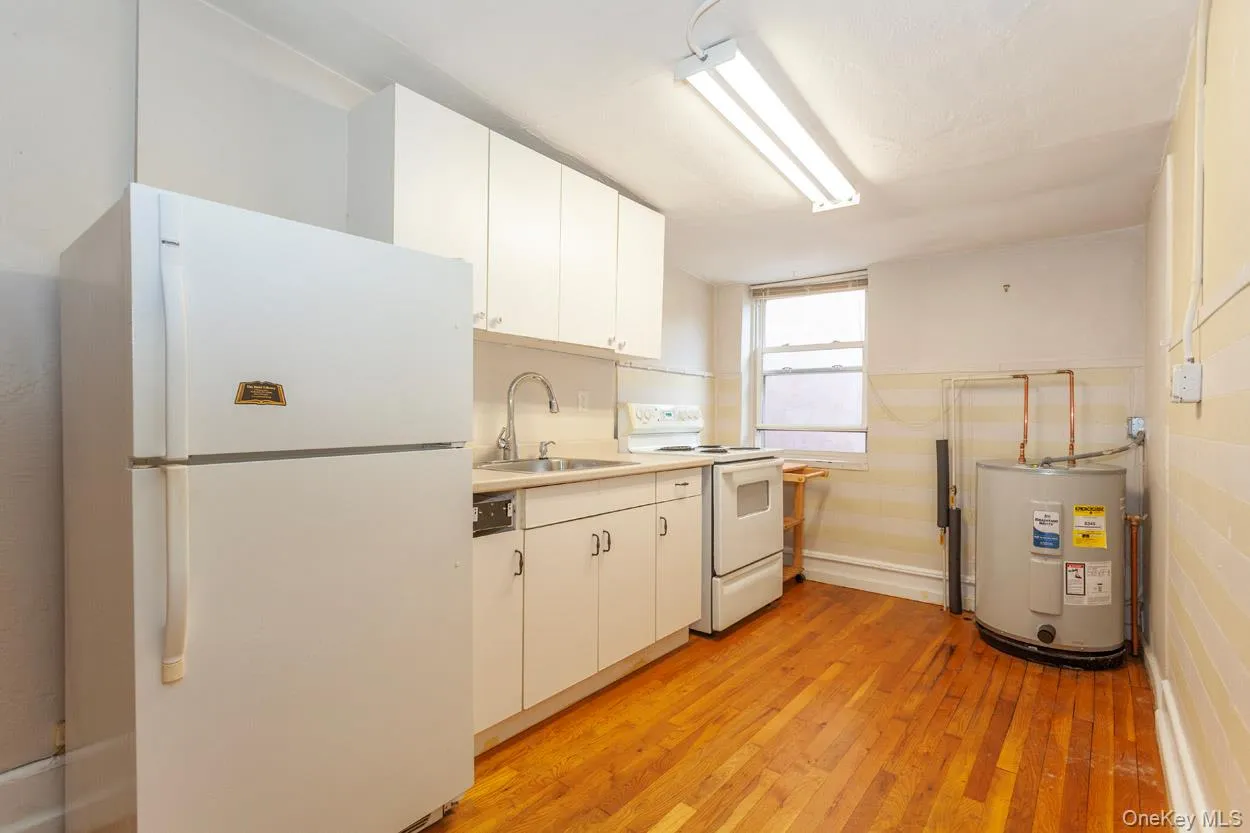 Kitchen featuring white appliances, light wood-style floors, light countertops, white cabinets, and water heater Kitchen featuring white appliances, light wood-style floors, light countertops, white cabinets, and water heater