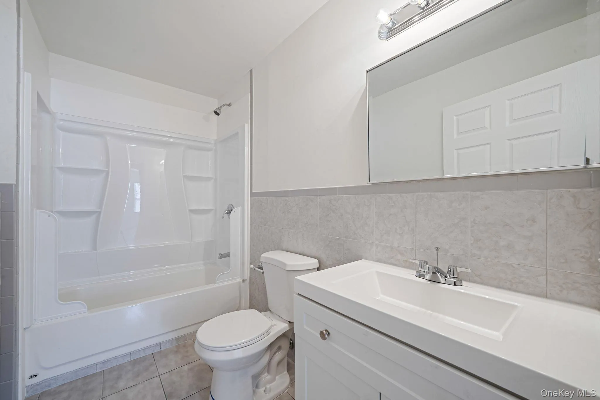 Full bath with tile walls, vanity, light tile patterned floors, washtub / shower combination, and wainscoting Full bath with tile walls, vanity, light tile patterned floors, washtub / shower combination, and wainscoting