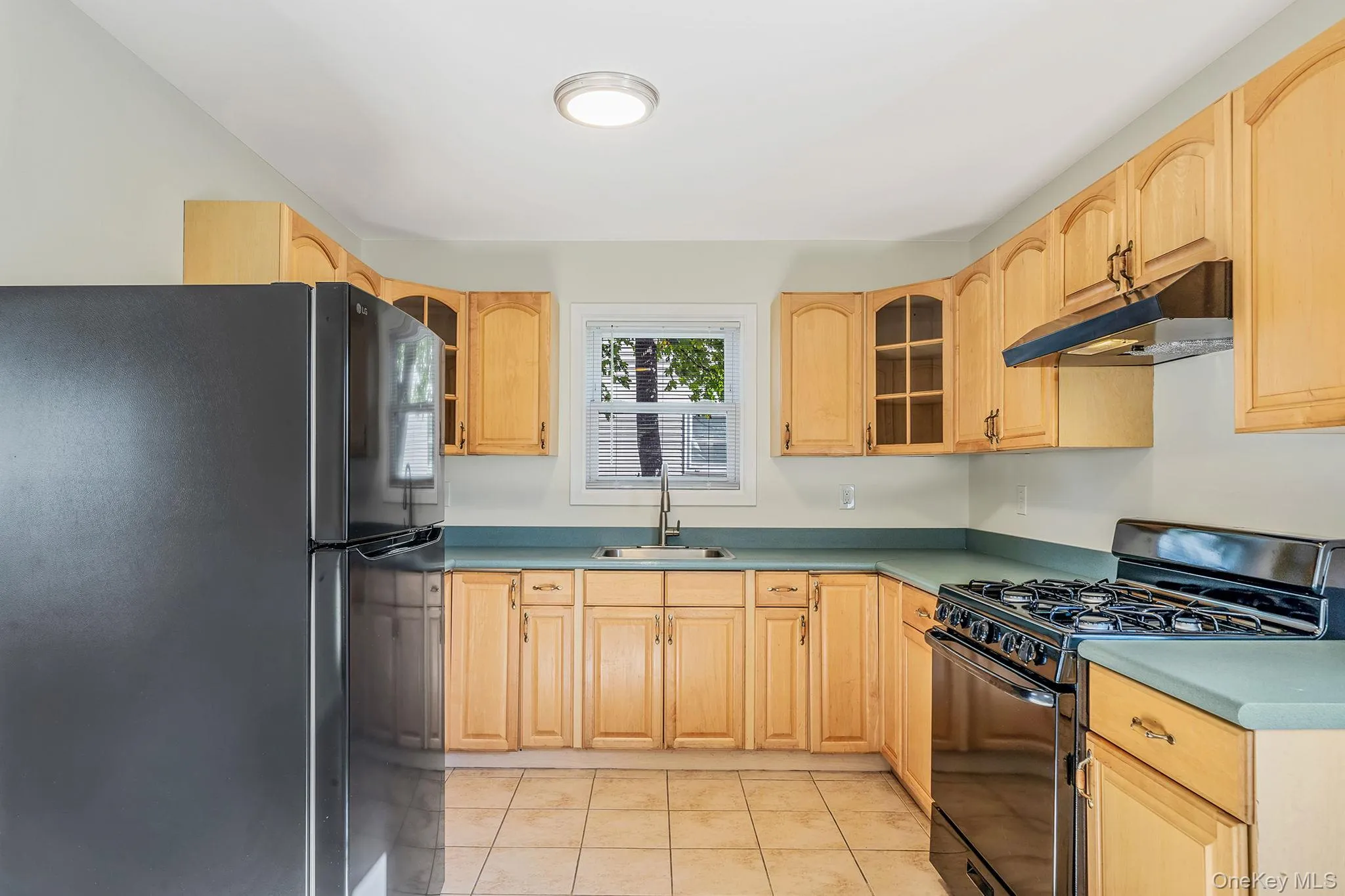 Kitchen with black appliances, glass insert cabinets, under cabinet range hood, and light tile patterned floors Kitchen with black appliances, glass insert cabinets, under cabinet range hood, and light tile patterned floors