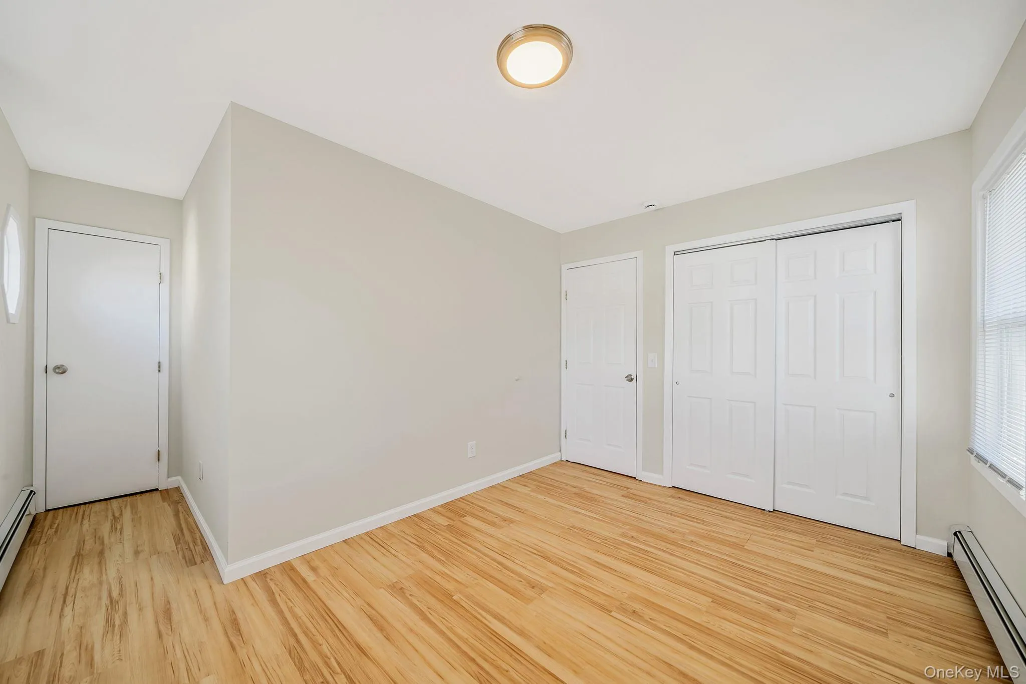 Unfurnished bedroom featuring a baseboard heating unit, light wood finished floors, and a closet Unfurnished bedroom featuring a baseboard heating unit, light wood finished floors, and a closet