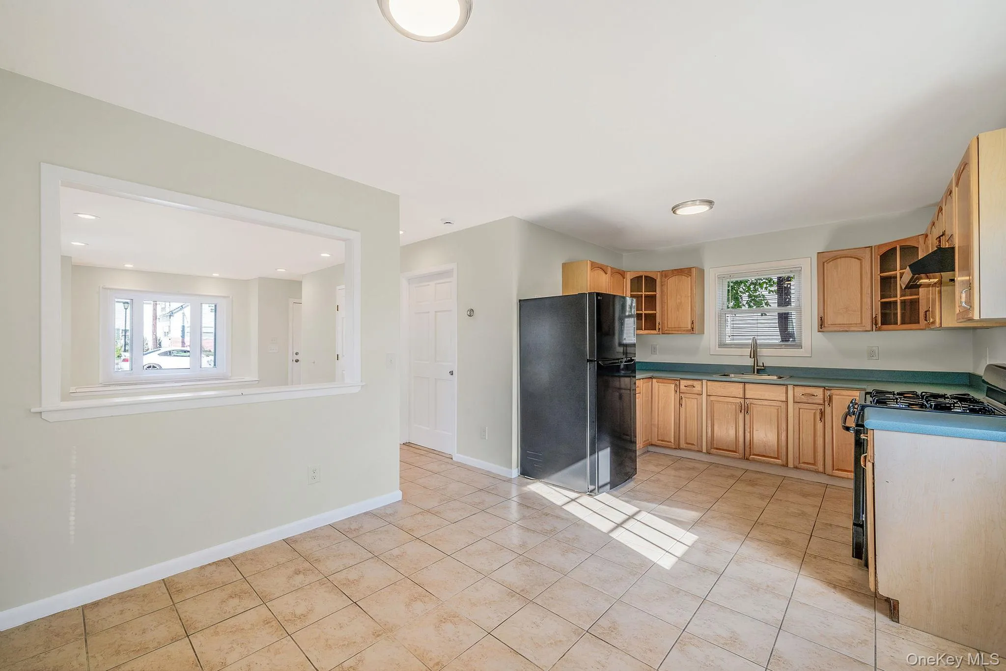 Kitchen featuring freestanding refrigerator, glass insert cabinets, range with gas stovetop, dark countertops, and light tile patterned floors Kitchen featuring freestanding refrigerator, glass insert cabinets, range with gas stovetop, dark countertops, and light tile patterned floors
