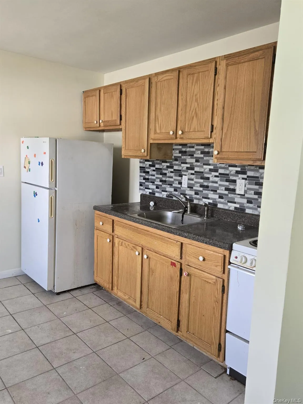 Kitchen with white appliances, backsplash, light tile patterned flooring, and brown cabinets Kitchen with white appliances, backsplash, light tile patterned flooring, and brown cabinets