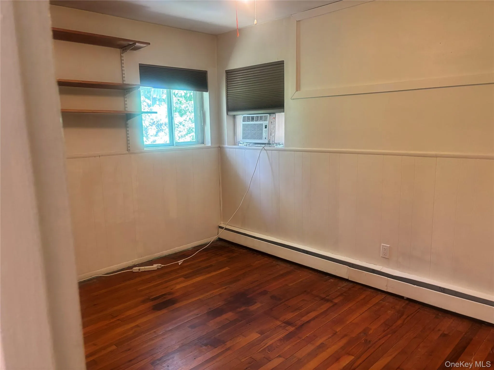 second bedroom wainscoting, baseboard heating, dark wood-type flooring, cooling unit, and wood walls second bedroom wainscoting, baseboard heating, dark wood-type flooring, cooling unit, and wood walls