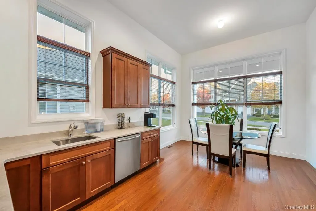 Kitchen featuring light wood-style flooring, stainless steel dishwasher, brown cabinetry, and light stone countertops Kitchen featuring light wood-style flooring, stainless steel dishwasher, brown cabinetry, and light stone countertops