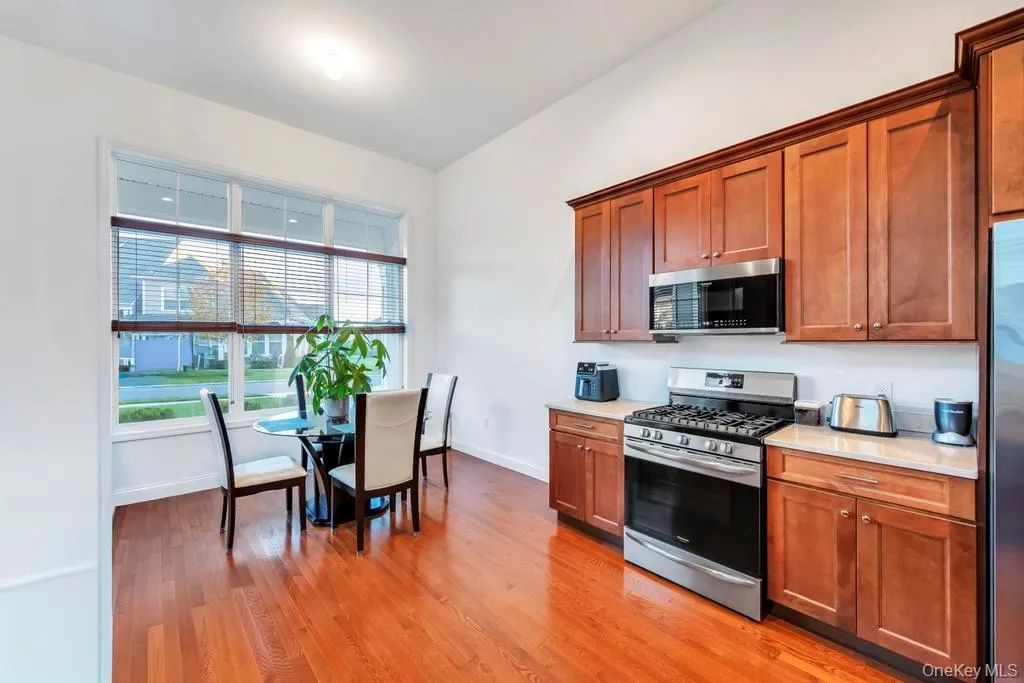 Kitchen with stainless steel appliances, light wood-type flooring, brown cabinetry, and light stone counters Kitchen with stainless steel appliances, light wood-type flooring, brown cabinetry, and light stone counters