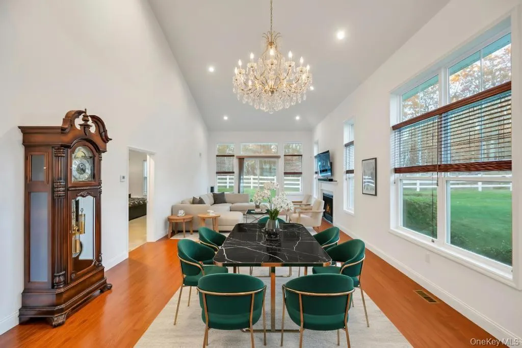 Dining area with a chandelier, light wood finished floors, a lit fireplace, a high ceiling, and recessed lighting Dining area with a chandelier, light wood finished floors, a lit fireplace, a high ceiling, and recessed lighting