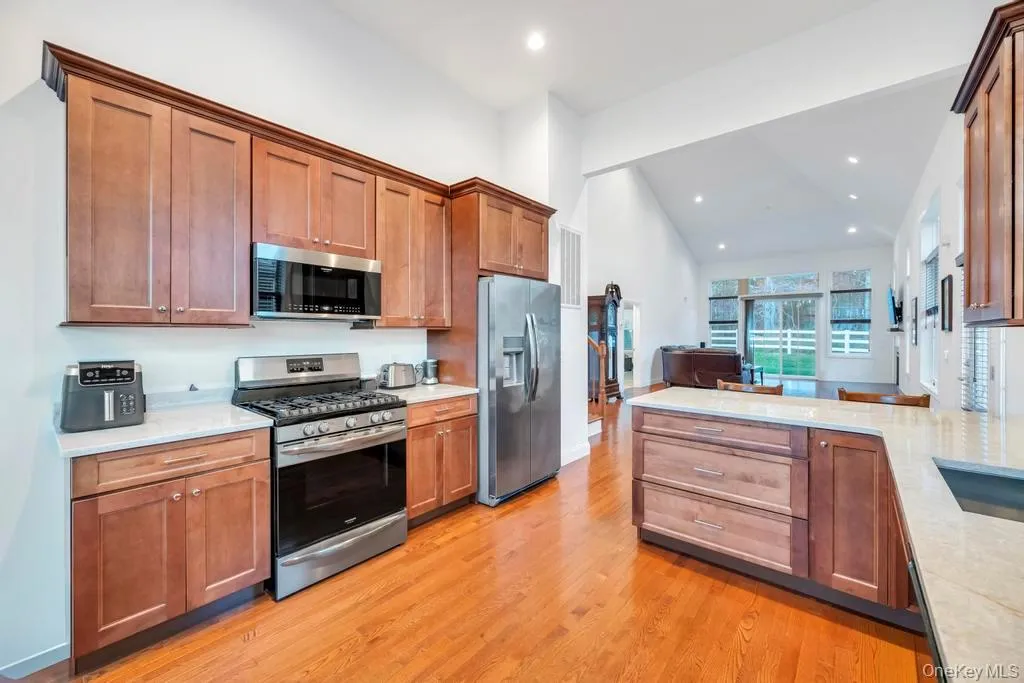 Kitchen featuring appliances with stainless steel finishes, brown cabinetry, light stone counters, a peninsula, and light wood-style floors Kitchen featuring appliances with stainless steel finishes, brown cabinetry, light stone counters, a peninsula, and light wood-style floors