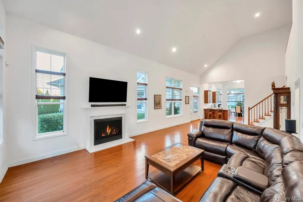 Living area with high vaulted ceiling, wood finished floors, recessed lighting, a lit fireplace, and stairs Living area with high vaulted ceiling, wood finished floors, recessed lighting, a lit fireplace, and stairs