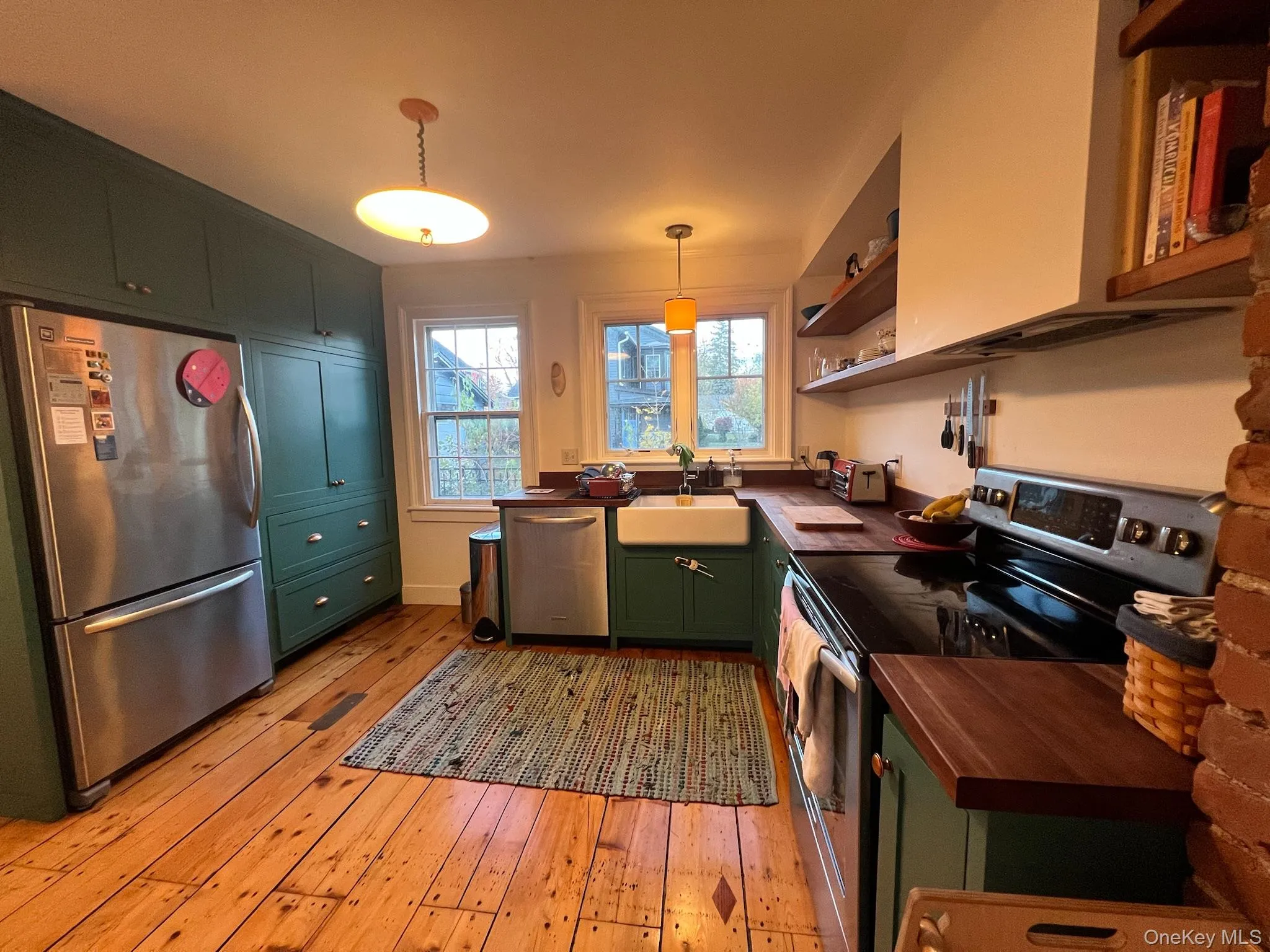 Kitchen with green cabinetry, stainless steel appliances, light wood finished floors, open shelves, and decorative light fixtures Kitchen with green cabinetry, stainless steel appliances, light wood finished floors, open shelves, and decorative light fixtures