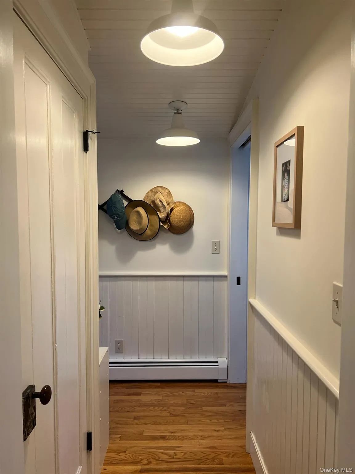 Hallway with wainscoting, a baseboard radiator, and wood finished floors Hallway with wainscoting, a baseboard radiator, and wood finished floors