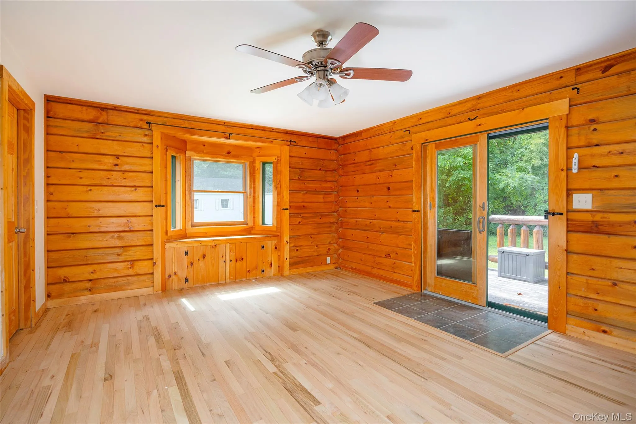 Unfurnished room featuring wood finished floors, healthy amount of natural light, a ceiling fan, and wooden walls Unfurnished room featuring wood finished floors, healthy amount of natural light, a ceiling fan, and wooden walls