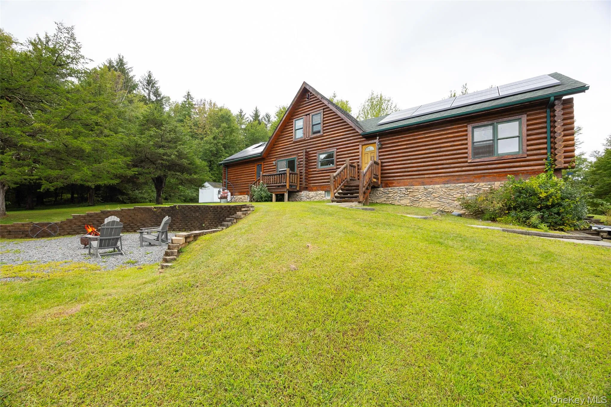 Rear view of property featuring solar panels, an outdoor fire pit, log siding, a patio, and a yard Rear view of property featuring solar panels, an outdoor fire pit, log siding, a patio, and a yard