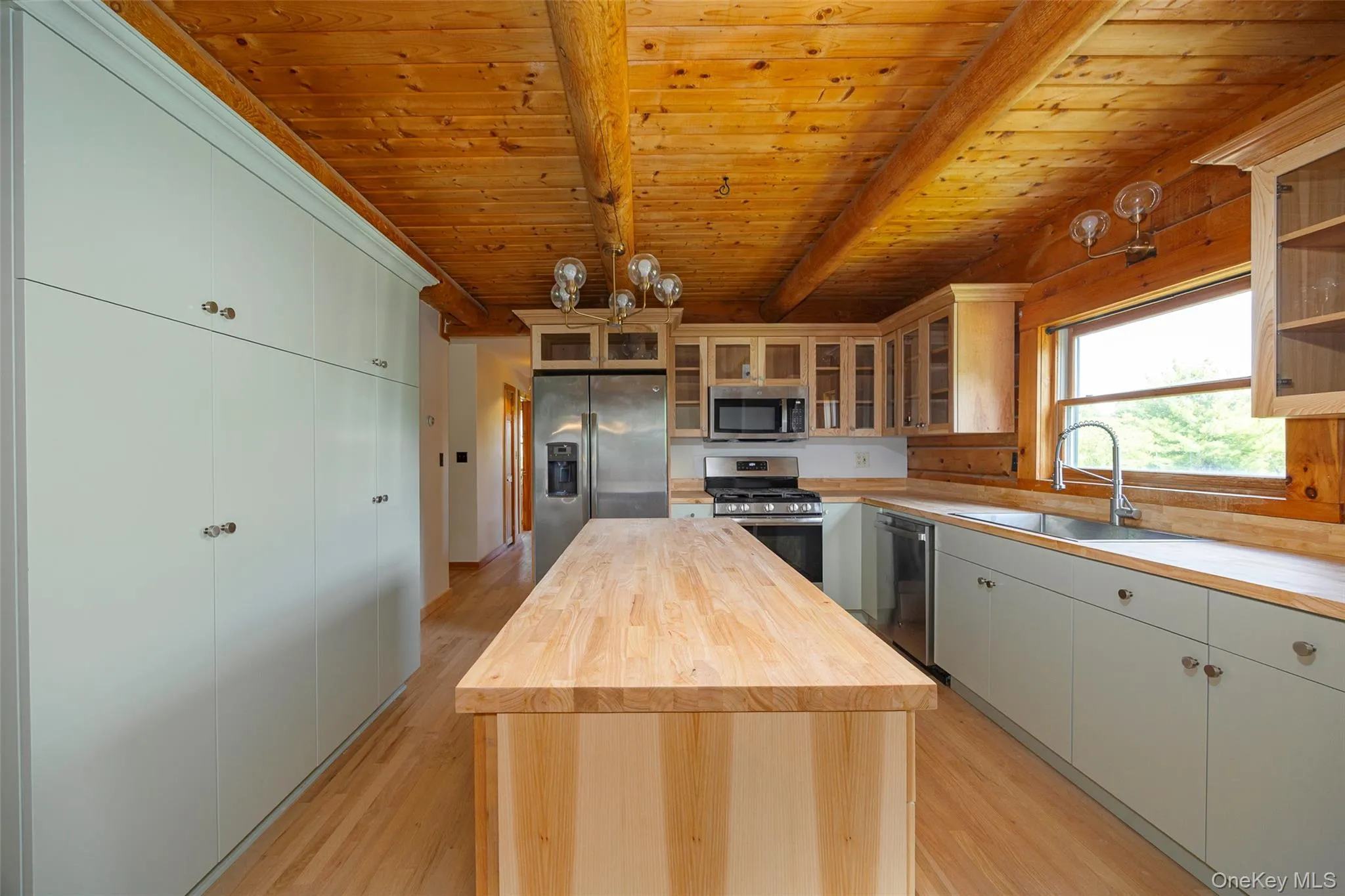 Kitchen featuring butcher block counters, light wood-style flooring, stainless steel appliances, glass insert cabinets, and a wooden ceiling with exposed beams Kitchen featuring butcher block counters, light wood-style flooring, stainless steel appliances, glass insert cabinets, and a wooden ceiling with exposed beams