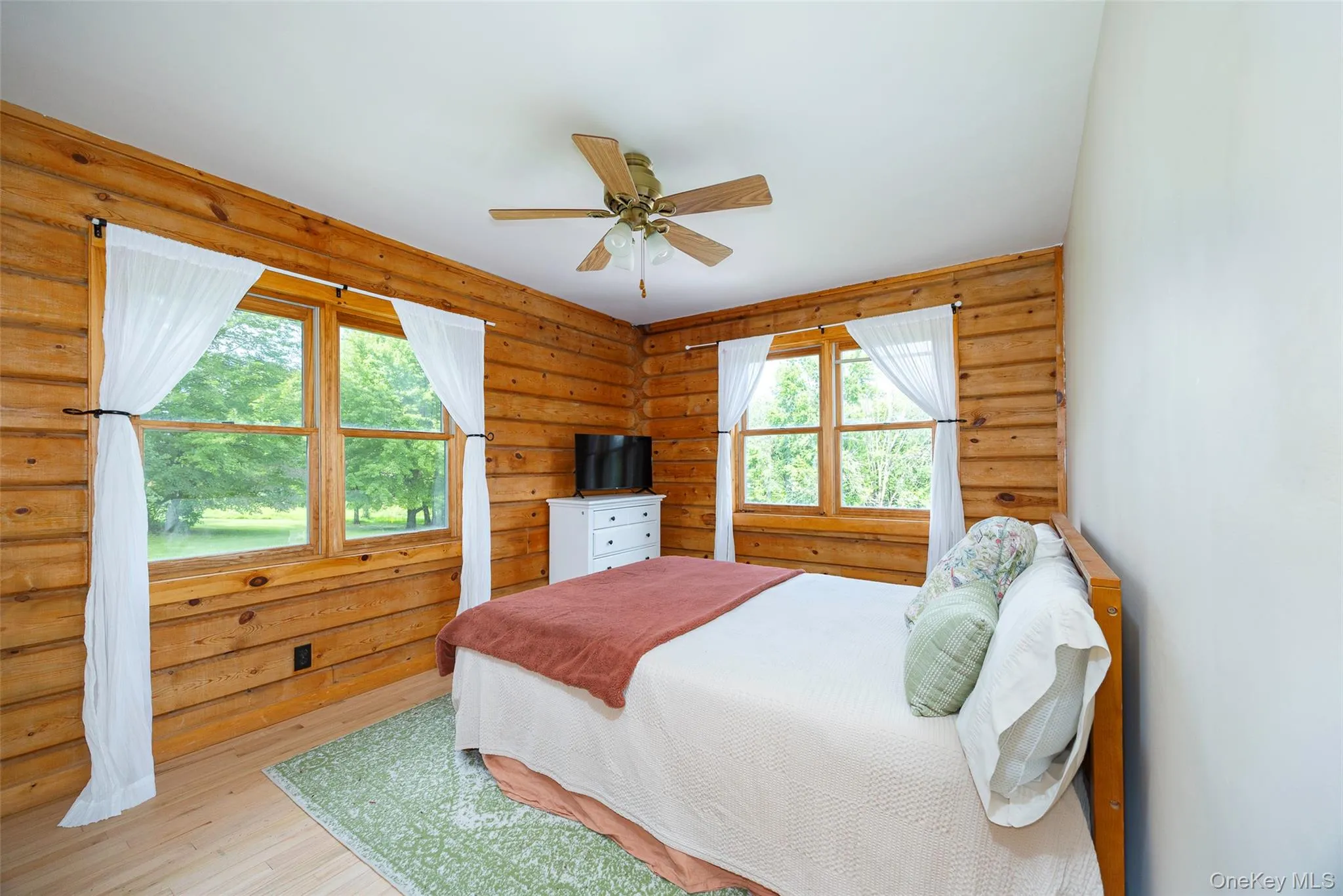 Bedroom with log walls, wood-type flooring, and ceiling fan Bedroom with log walls, wood-type flooring, and ceiling fan
