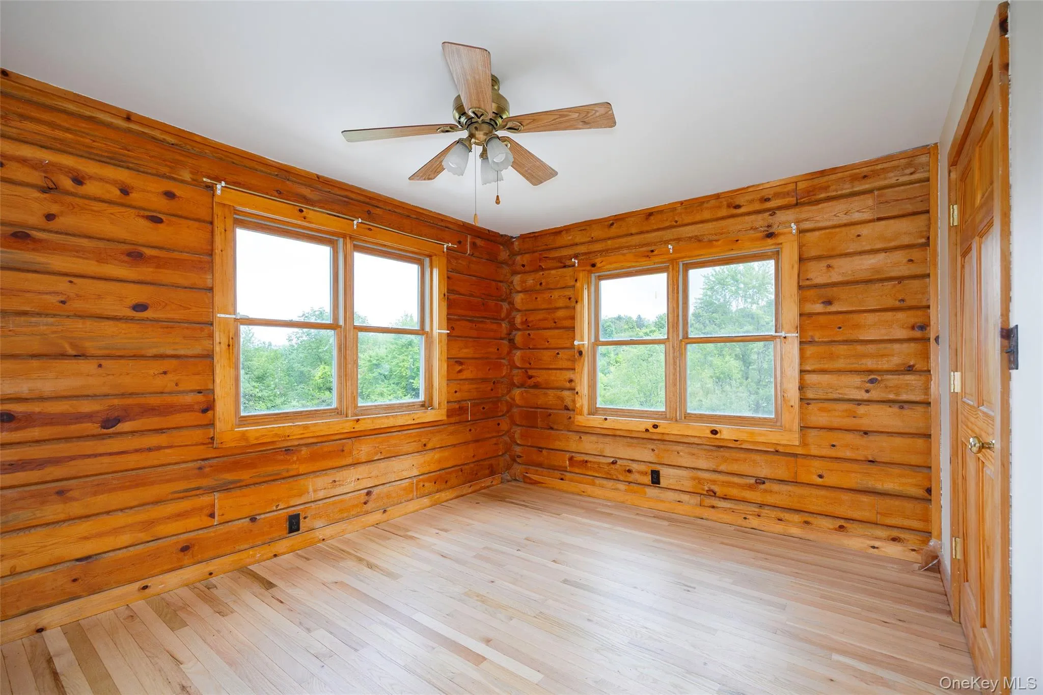 Empty room featuring log walls, wood-type flooring, plenty of natural light, and ceiling fan Empty room featuring log walls, wood-type flooring, plenty of natural light, and ceiling fan