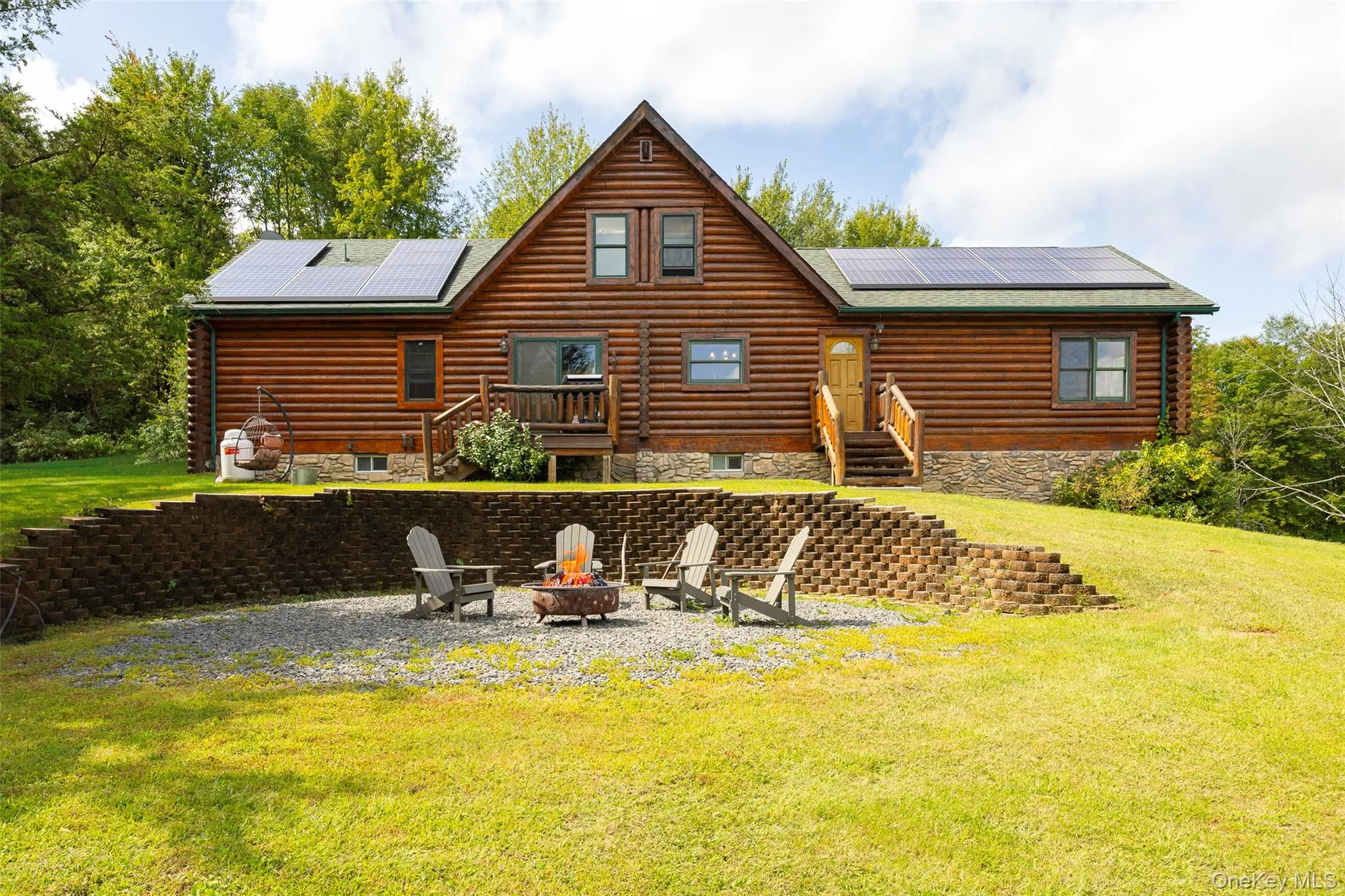 Back of property featuring solar panels, a yard, log exterior, and a patio area Back of property featuring solar panels, a yard, log exterior, and a patio area
