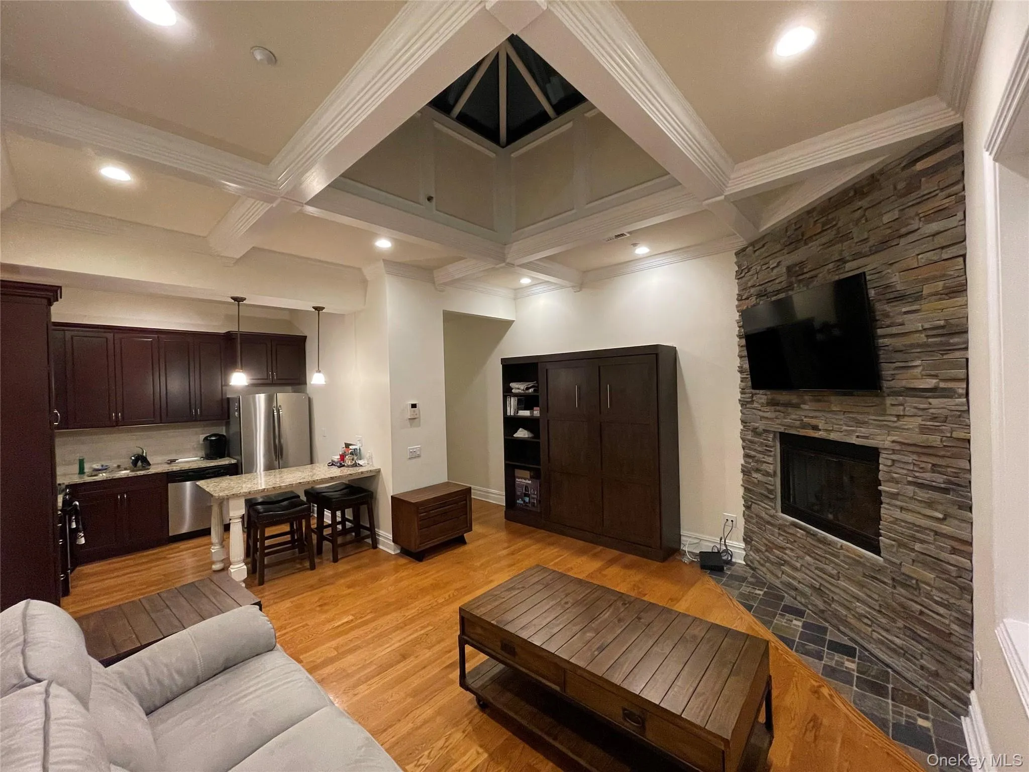 Living area featuring coffered ceiling, light wood-style floors, beamed ceiling, a fireplace, and crown molding Living area featuring coffered ceiling, light wood-style floors, beamed ceiling, a fireplace, and crown molding