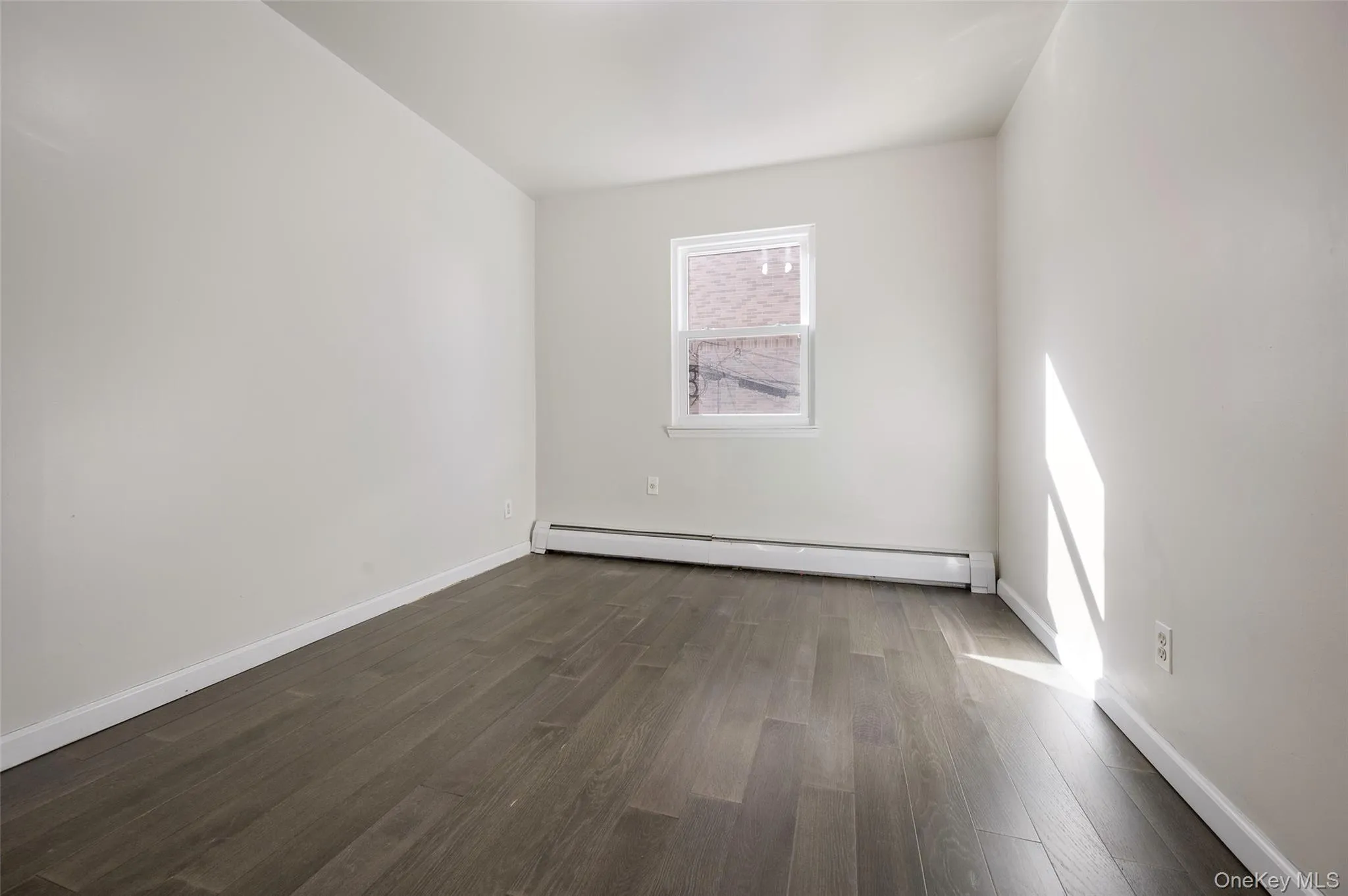 Unfurnished room featuring dark wood-style flooring and a baseboard radiator Unfurnished room featuring dark wood-style flooring and a baseboard radiator