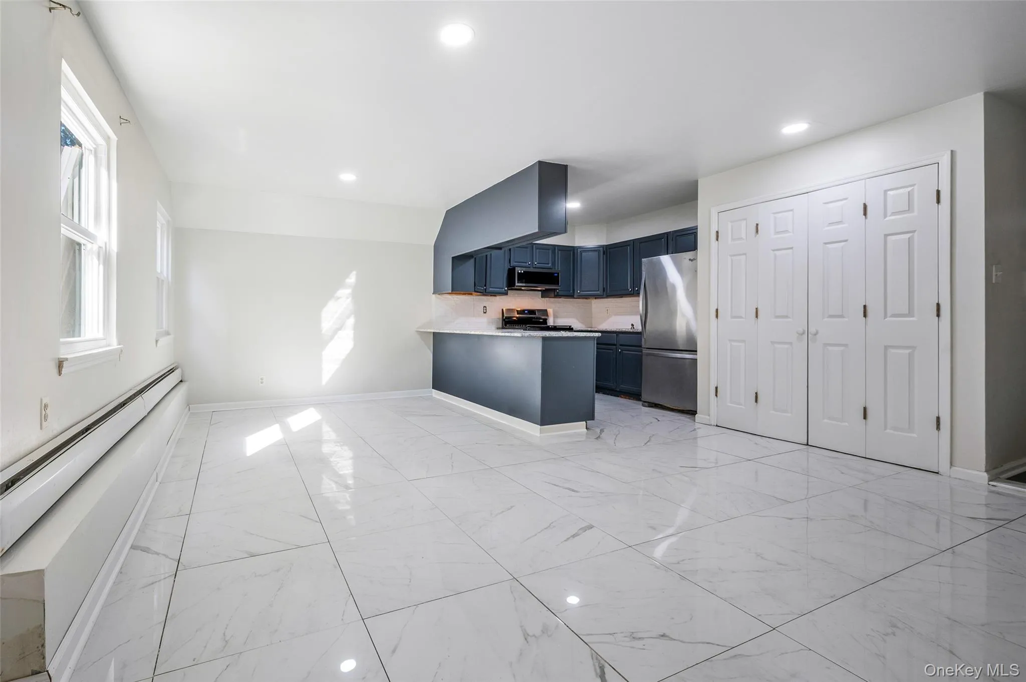 Kitchen featuring blue cabinetry, light marble finish floors, appliances with stainless steel finishes, light countertops, and backsplash Kitchen featuring blue cabinetry, light marble finish floors, appliances with stainless steel finishes, light countertops, and backsplash