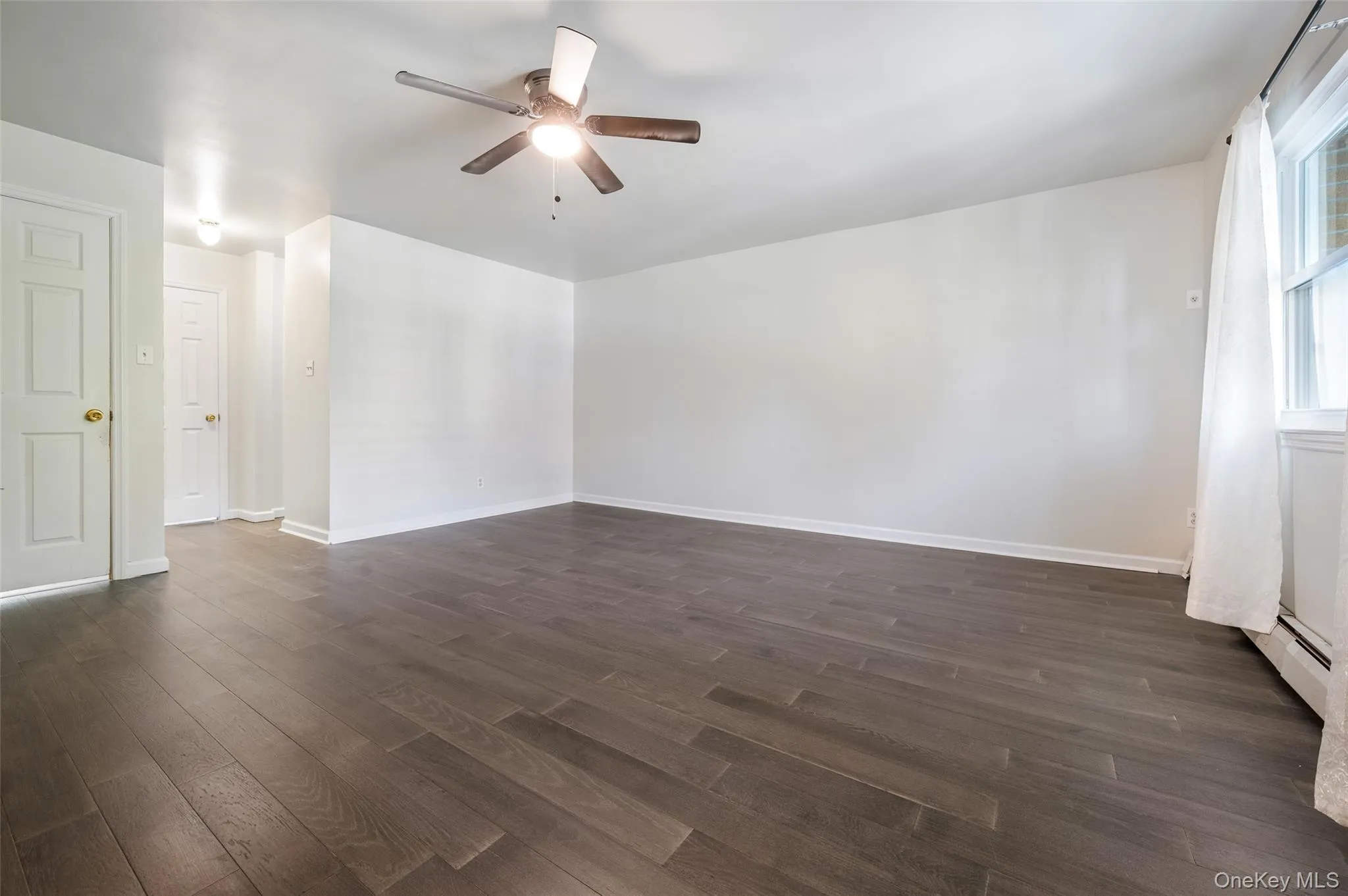 Spare room featuring dark wood-style floors, ceiling fan, and a baseboard radiator Spare room featuring dark wood-style floors, ceiling fan, and a baseboard radiator