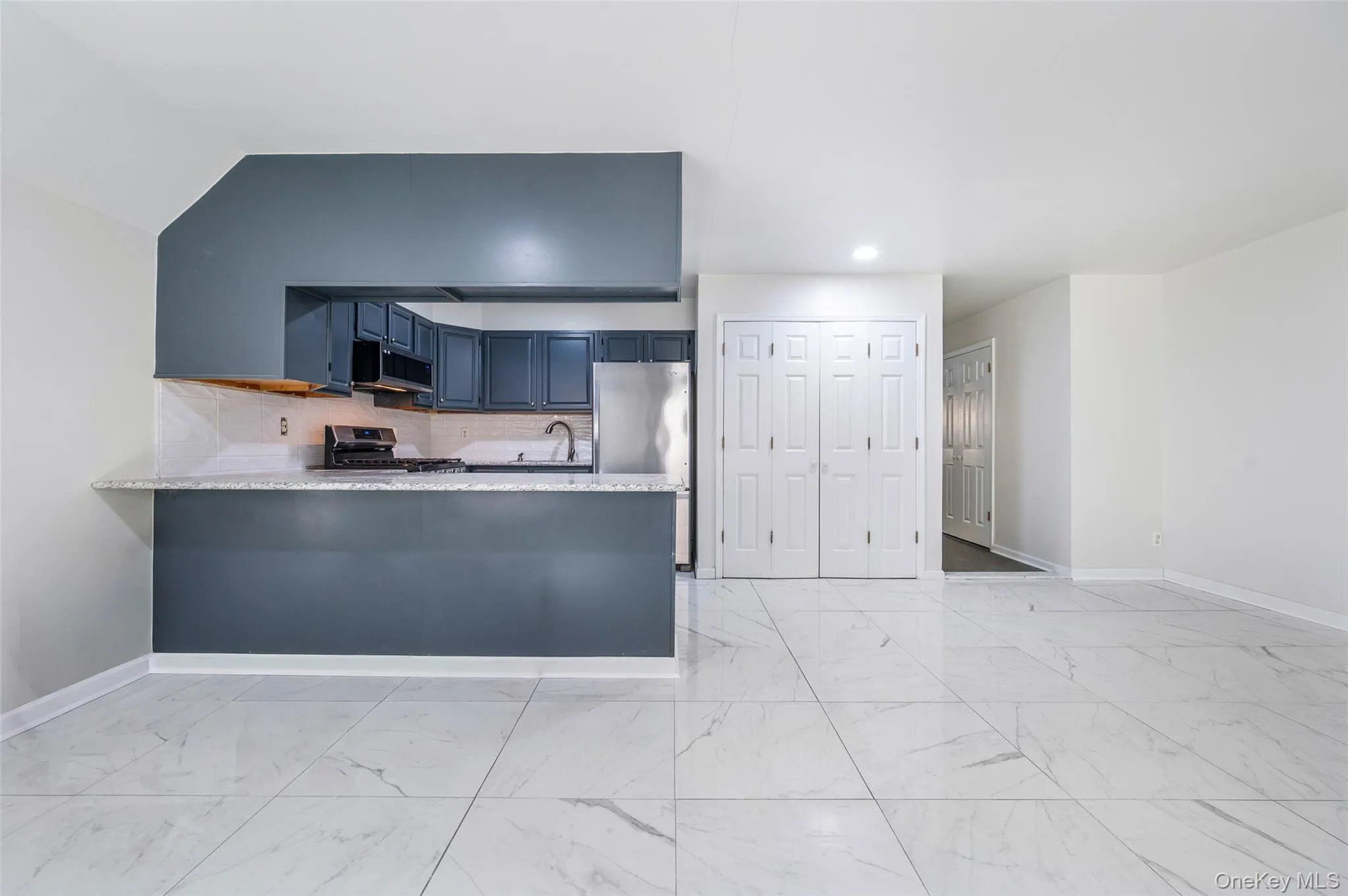 Kitchen with backsplash, light marble finish flooring, a peninsula, and appliances with stainless steel finishes Kitchen with backsplash, light marble finish flooring, a peninsula, and appliances with stainless steel finishes