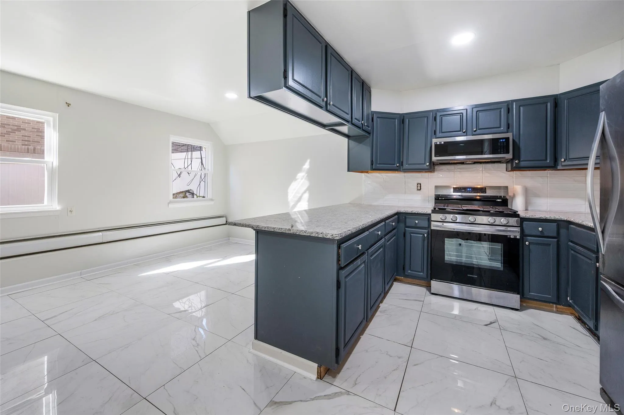 Kitchen featuring backsplash, light marble finish flooring, appliances with stainless steel finishes, light stone countertops, and a peninsula Kitchen featuring backsplash, light marble finish flooring, appliances with stainless steel finishes, light stone countertops, and a peninsula