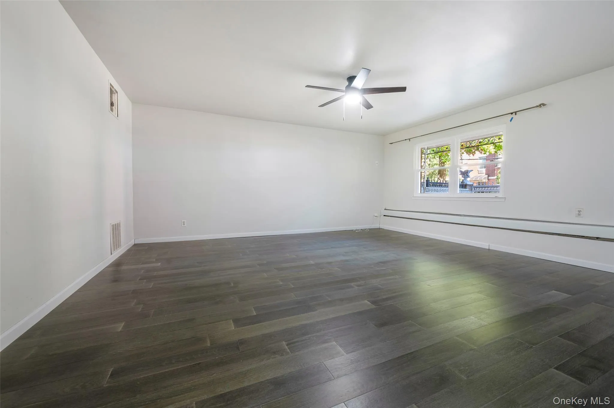 Unfurnished room featuring dark wood-type flooring, ceiling fan, and a baseboard radiator Unfurnished room featuring dark wood-type flooring, ceiling fan, and a baseboard radiator