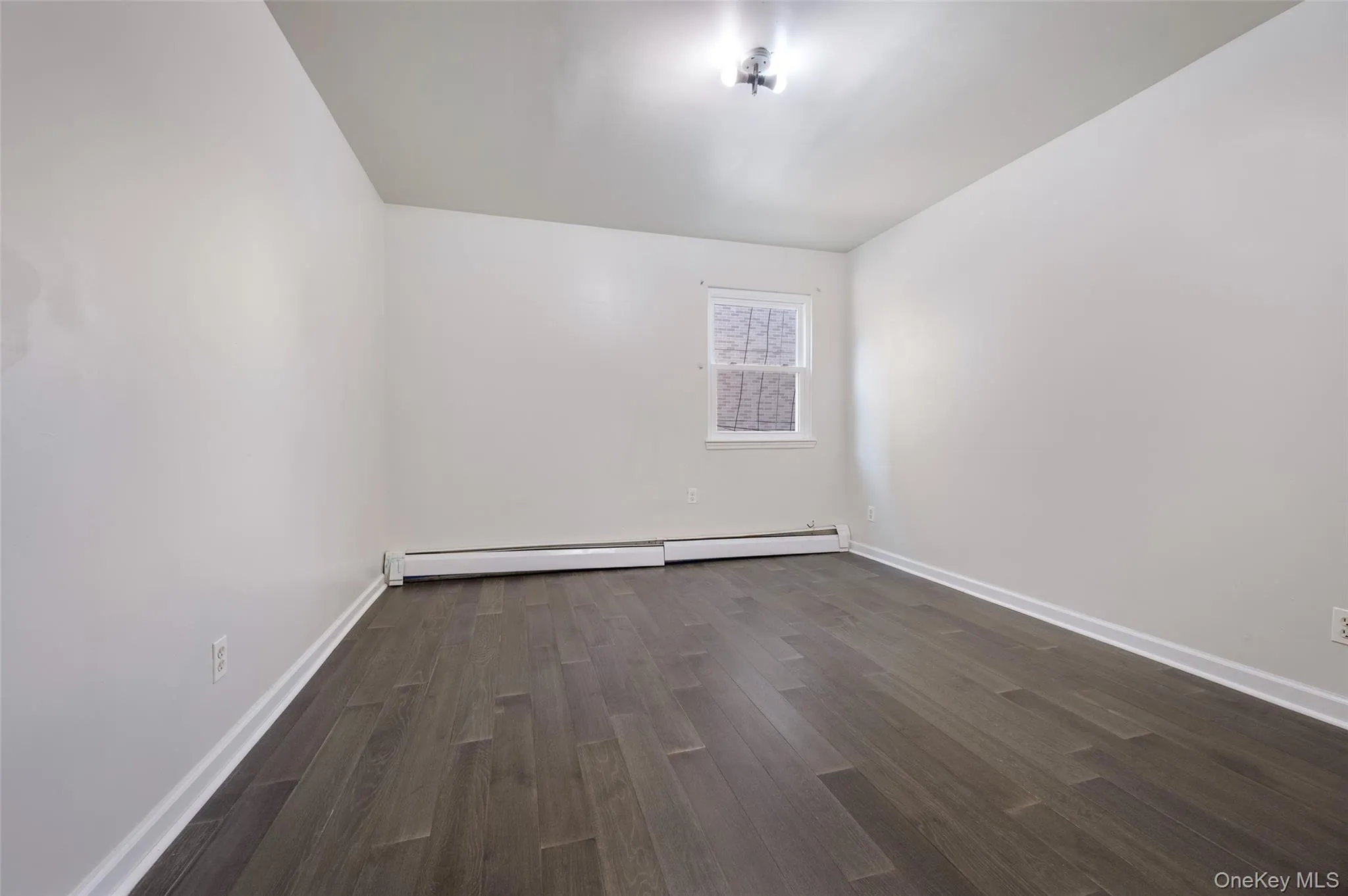 Unfurnished room featuring dark wood-style floors and a baseboard heating unit Unfurnished room featuring dark wood-style floors and a baseboard heating unit