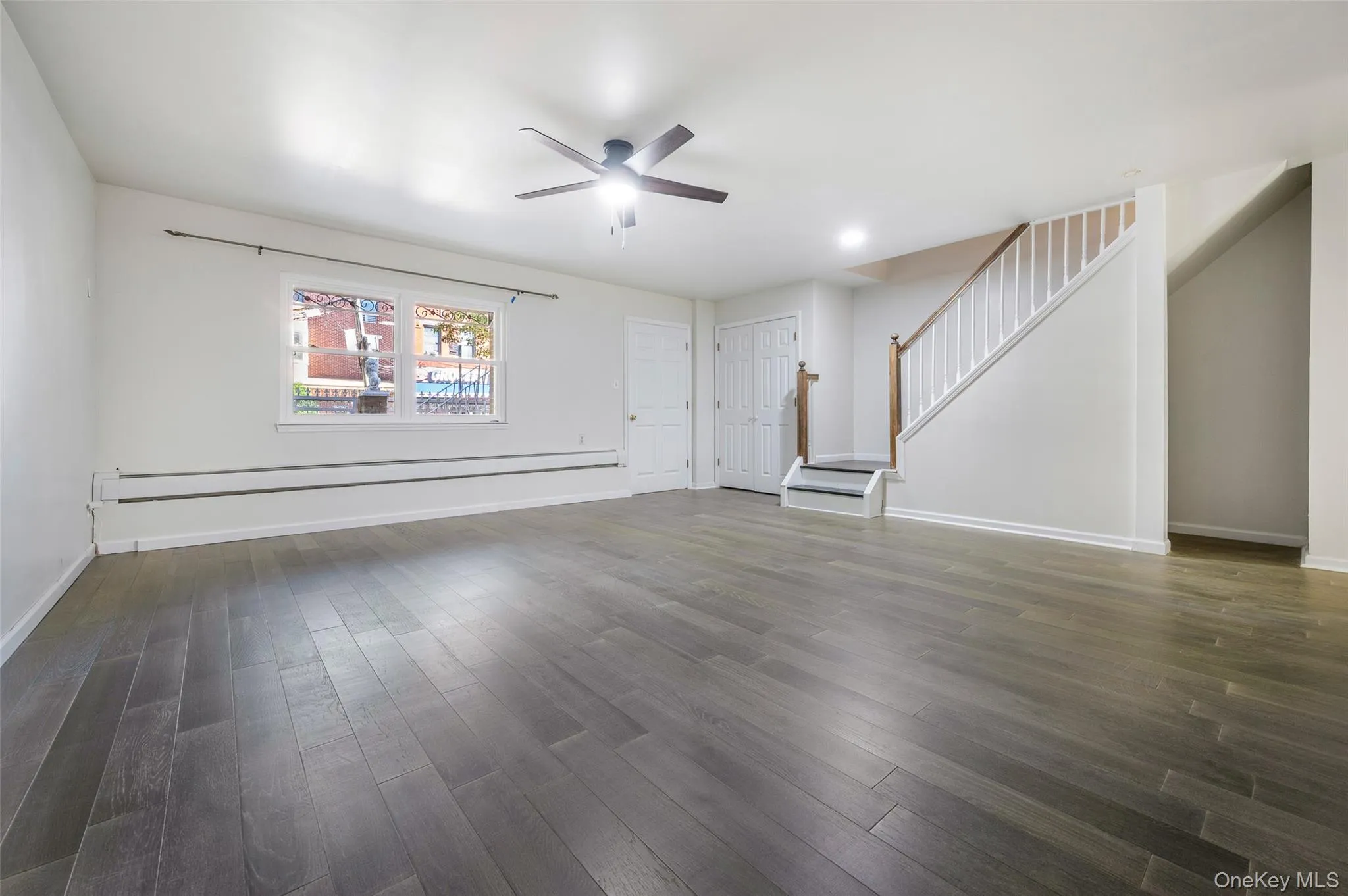 Unfurnished living room featuring dark wood finished floors, stairway, a baseboard radiator, and ceiling fan Unfurnished living room featuring dark wood finished floors, stairway, a baseboard radiator, and ceiling fan