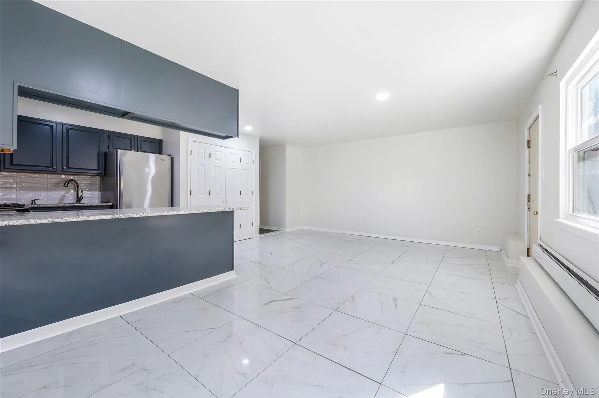 Kitchen featuring light marble finish floors, light stone countertops, freestanding refrigerator, backsplash, and a baseboard heating unit Kitchen featuring light marble finish floors, light stone countertops, freestanding refrigerator, backsplash, and a baseboard heating unit