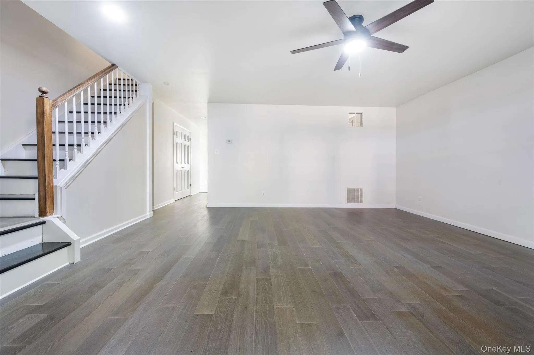 Unfurnished living room featuring stairway, dark wood-style floors, and a ceiling fan Unfurnished living room featuring stairway, dark wood-style floors, and a ceiling fan