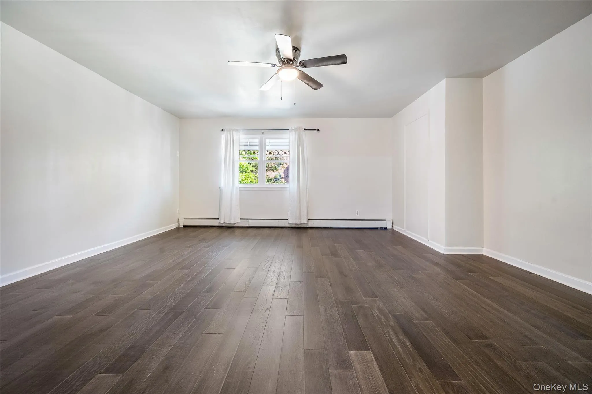 Spare room with dark wood-type flooring, a ceiling fan, and baseboard heating Spare room with dark wood-type flooring, a ceiling fan, and baseboard heating