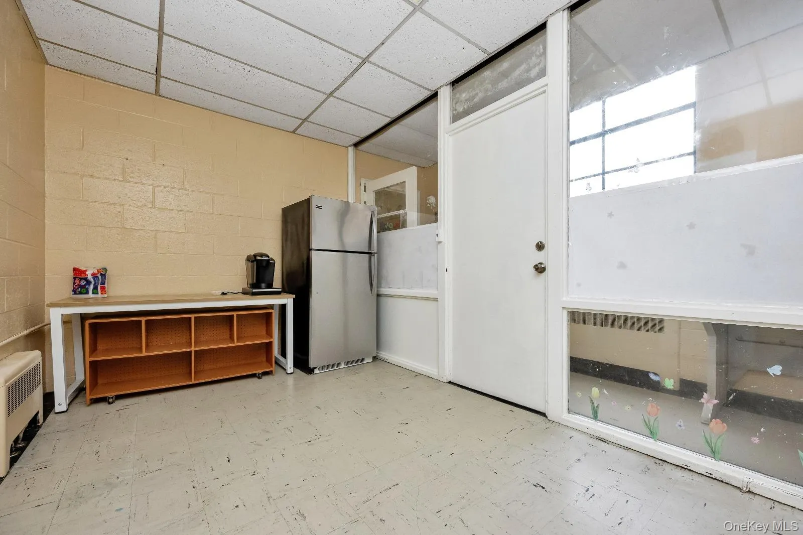 Miscellaneous room featuring light floors, concrete block wall, and a drop ceiling Miscellaneous room featuring light floors, concrete block wall, and a drop ceiling