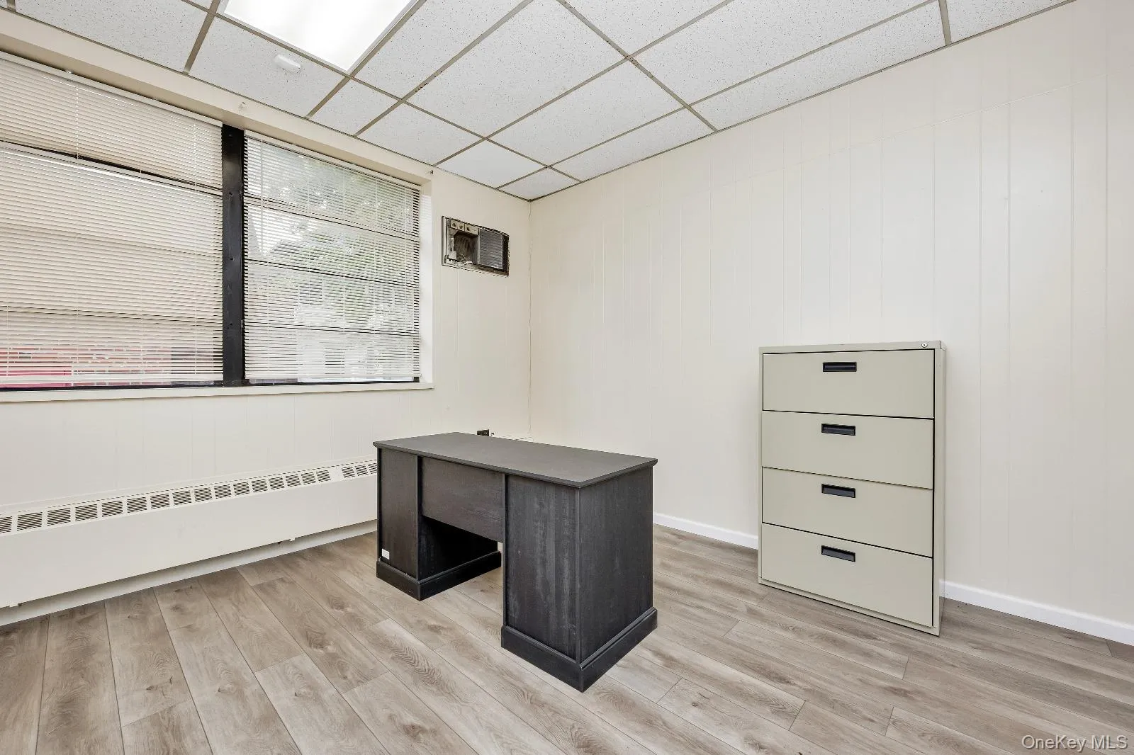 Unfurnished office with light wood-type flooring, a paneled ceiling, and a baseboard radiator Unfurnished office with light wood-type flooring, a paneled ceiling, and a baseboard radiator
