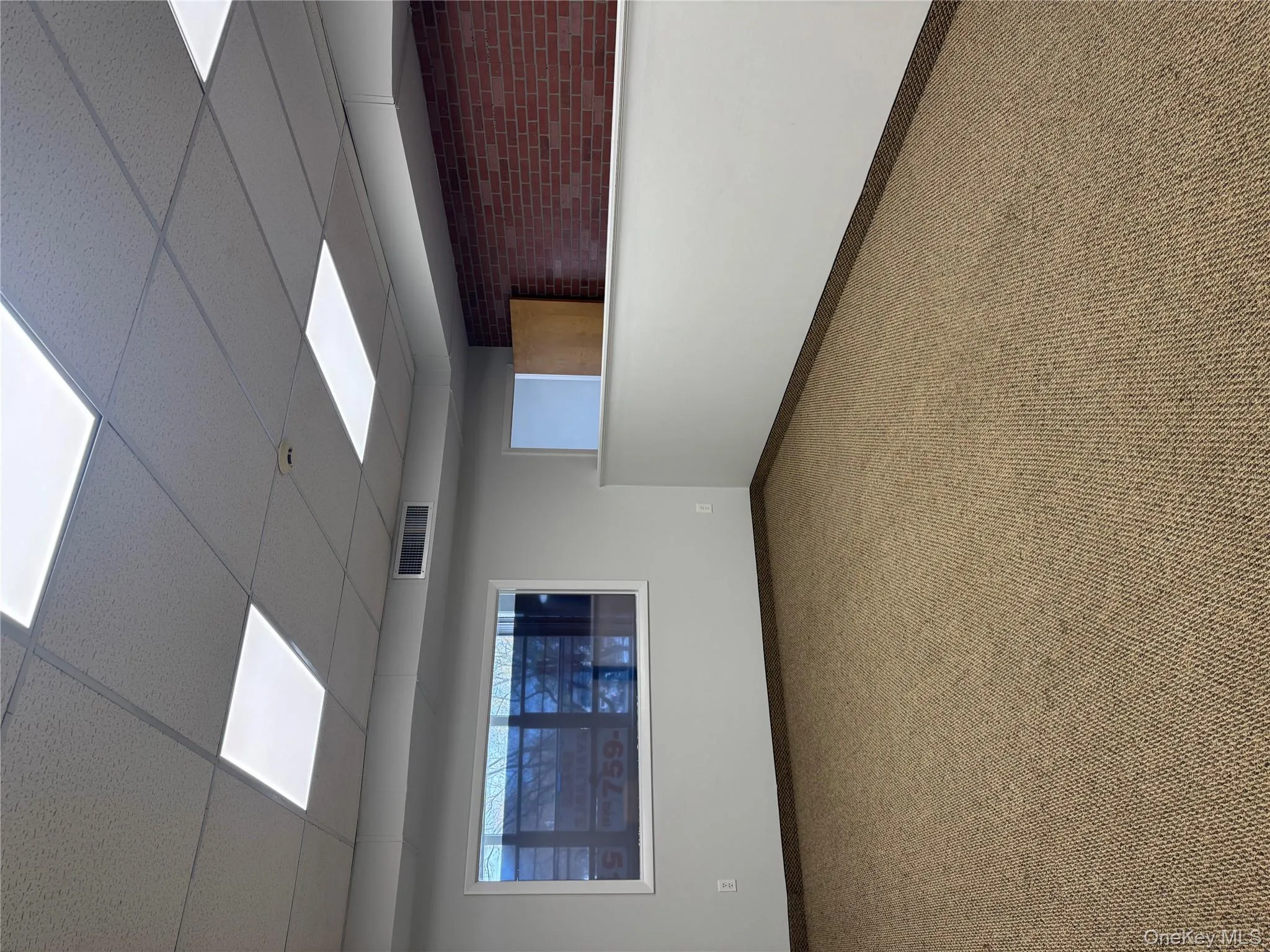 Spare room with a drop ceiling, carpet flooring, and brick wall Spare room with a drop ceiling, carpet flooring, and brick wall