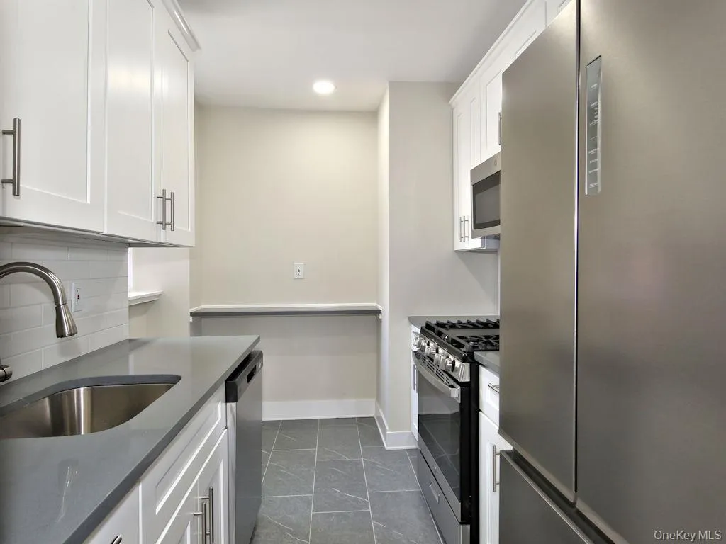 Kitchen with appliances with stainless steel finishes, decorative backsplash, white cabinetry, recessed lighting, and dark stone counters Kitchen with appliances with stainless steel finishes, decorative backsplash, white cabinetry, recessed lighting, and dark stone counters