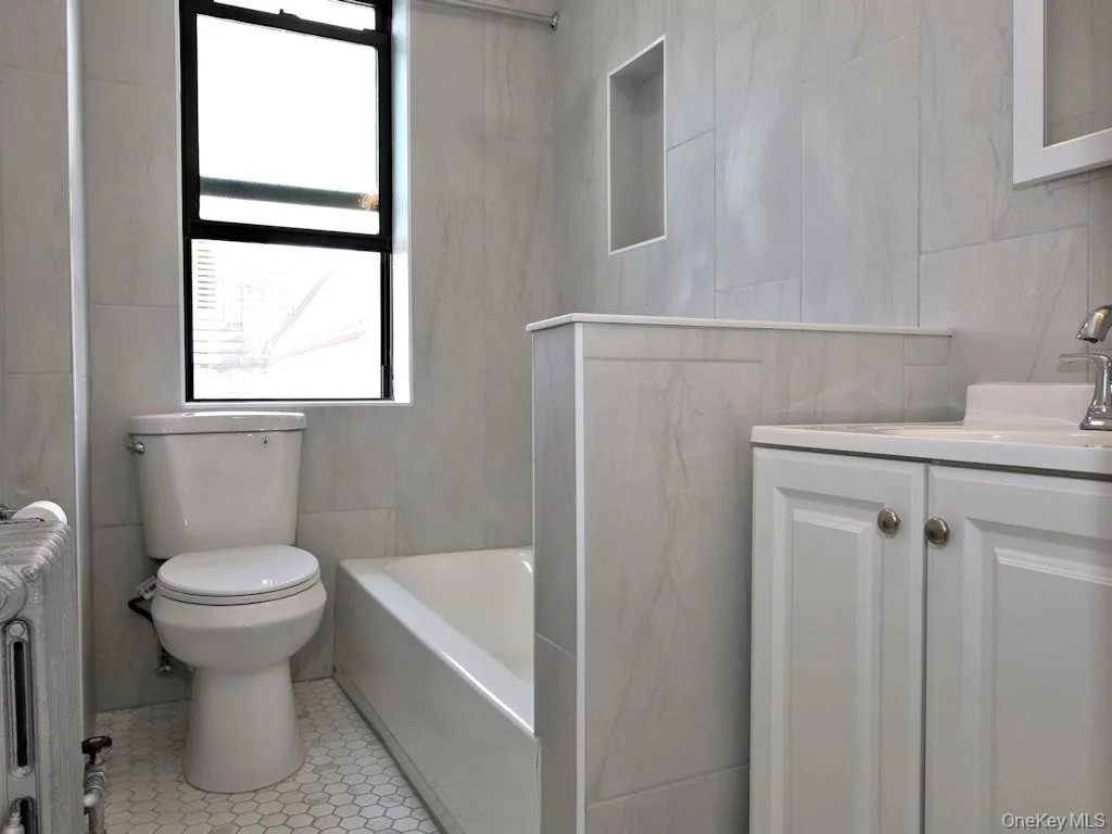 Full bath featuring tile walls, radiator heating unit, vanity, and washtub / shower combination Full bath featuring tile walls, radiator heating unit, vanity, and washtub / shower combination