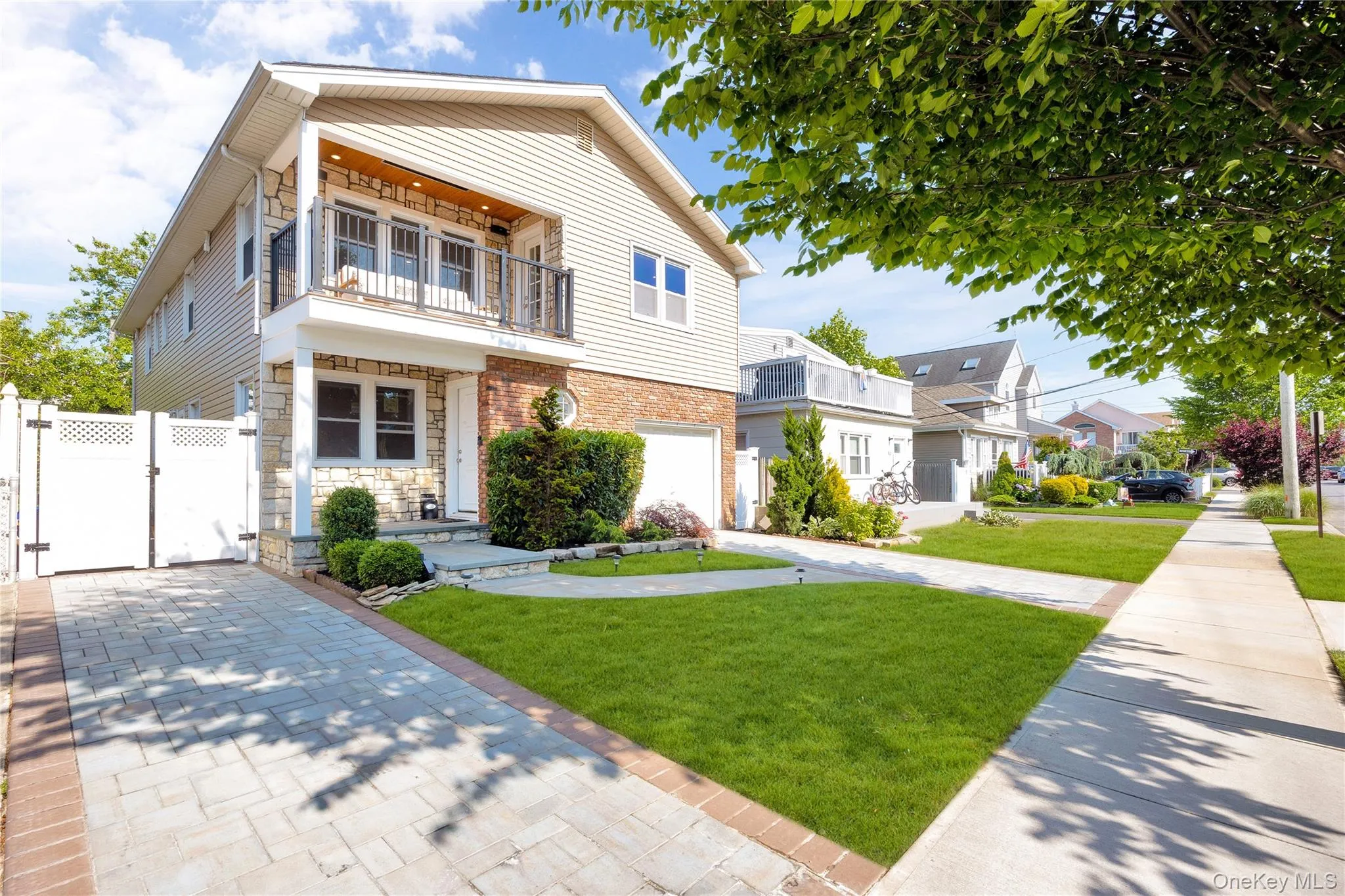 View of front facade featuring a gate, a balcony, stone siding, driveway, and a residential view View of front facade featuring a gate, a balcony, stone siding, driveway, and a residential view