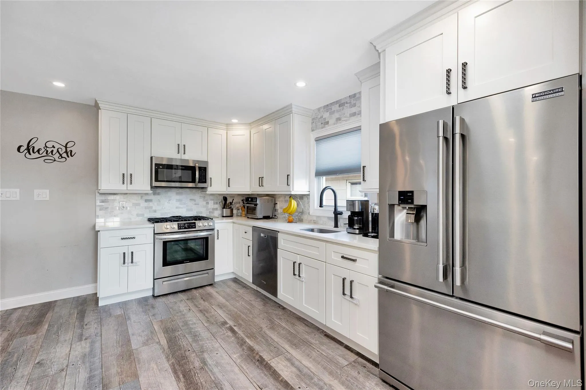 Kitchen featuring appliances with stainless steel finishes, white cabinetry, backsplash, light wood-type flooring, and recessed lighting Kitchen featuring appliances with stainless steel finishes, white cabinetry, backsplash, light wood-type flooring, and recessed lighting