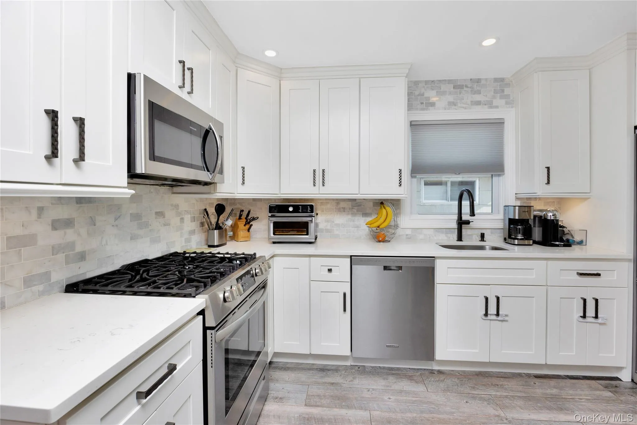 Kitchen with appliances with stainless steel finishes, tasteful backsplash, white cabinetry, light wood-type flooring, and light stone countertops Kitchen with appliances with stainless steel finishes, tasteful backsplash, white cabinetry, light wood-type flooring, and light stone countertops