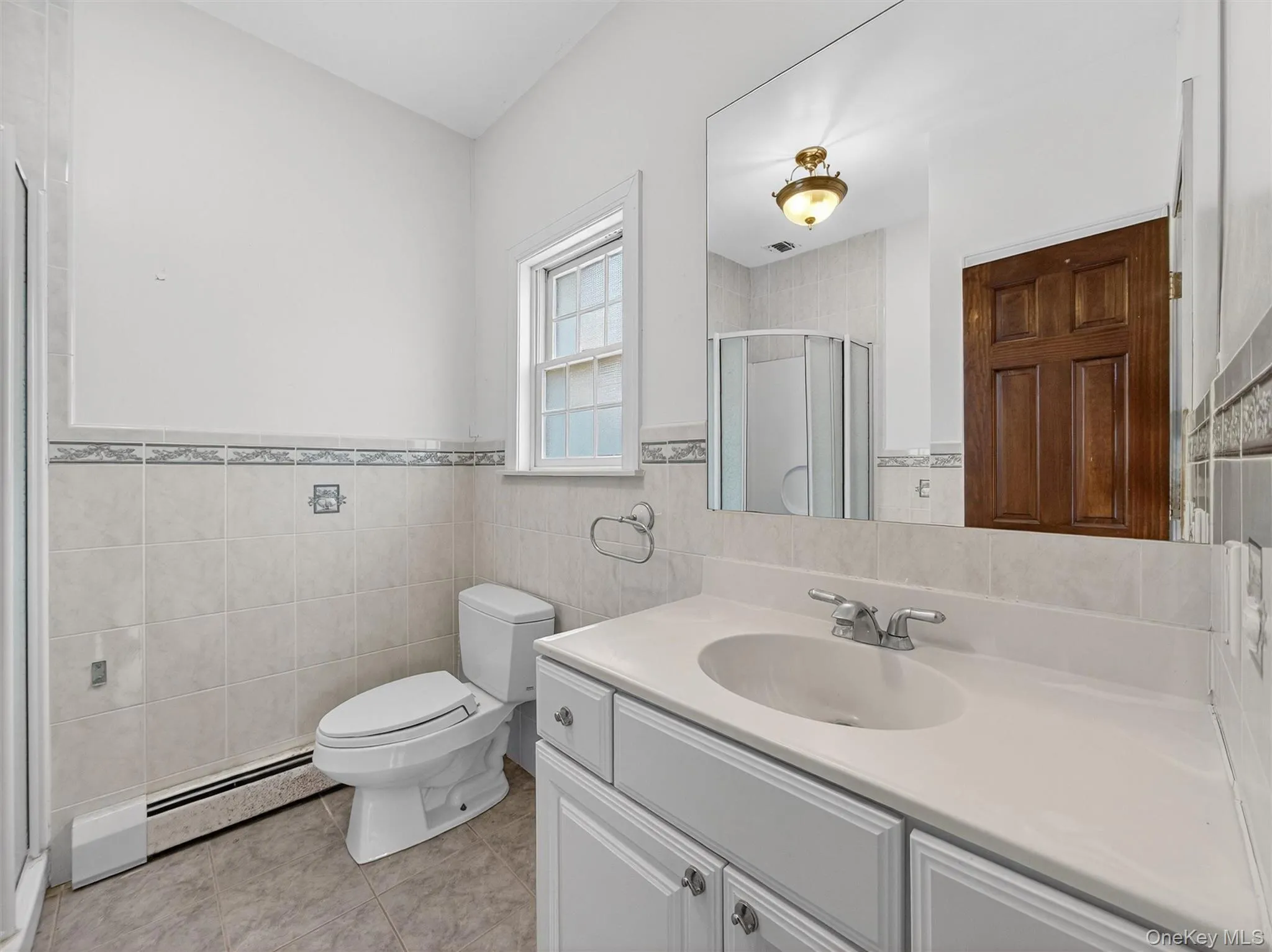Full bath with a stall shower, vanity, a baseboard radiator, tile walls, and light tile patterned floors Full bath with a stall shower, vanity, a baseboard radiator, tile walls, and light tile patterned floors