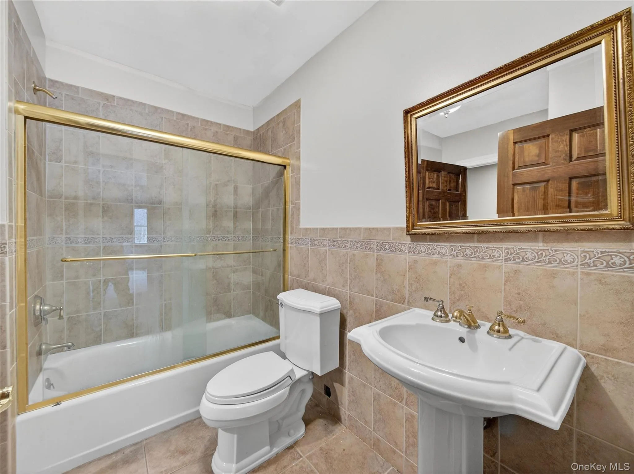Bathroom featuring tile walls, bath / shower combo with glass door, a wainscoted wall, and tile patterned floors Bathroom featuring tile walls, bath / shower combo with glass door, a wainscoted wall, and tile patterned floors