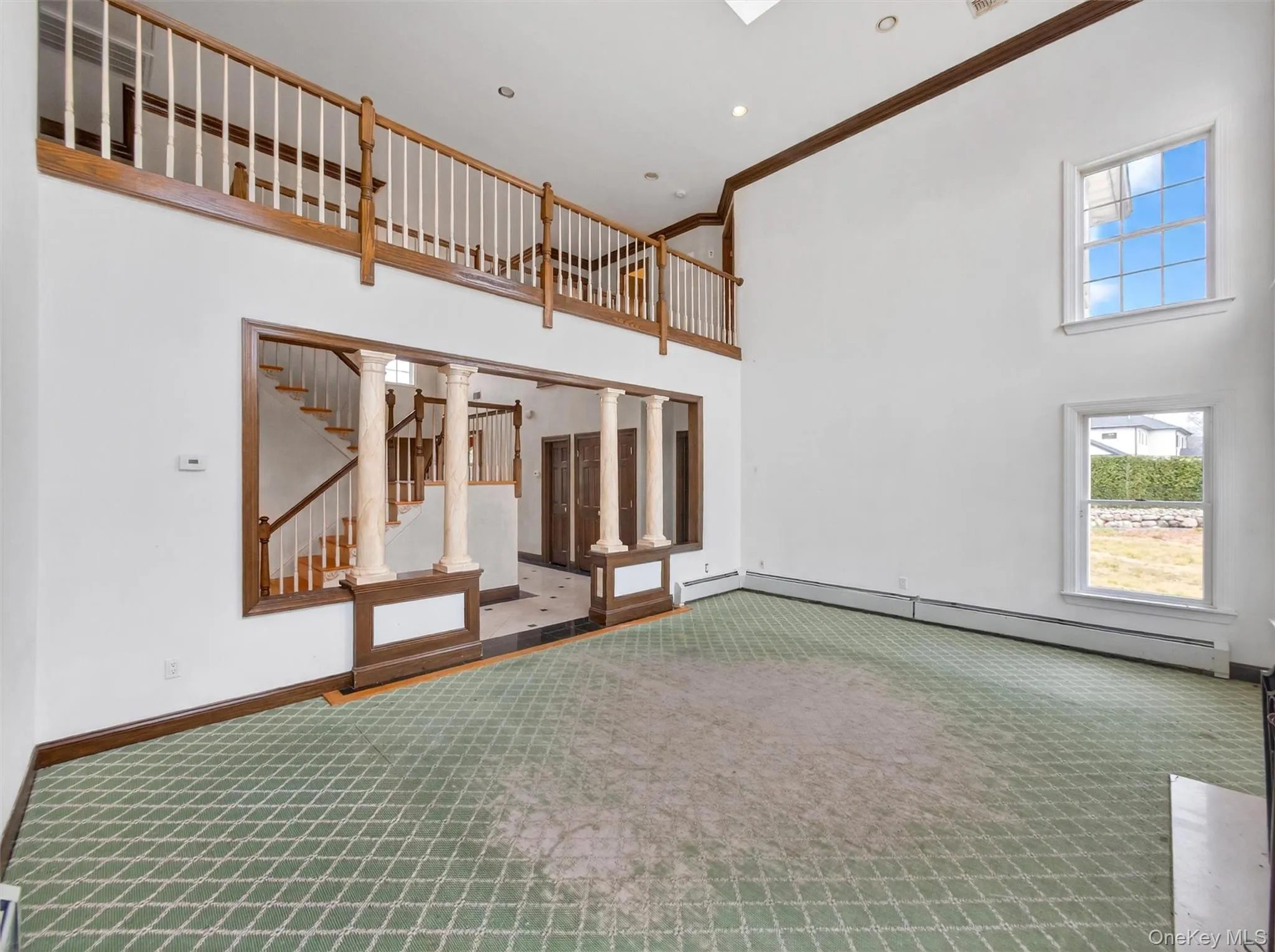 Unfurnished living room featuring a high ceiling, carpet flooring, a baseboard radiator, crown molding, and ornate columns Unfurnished living room featuring a high ceiling, carpet flooring, a baseboard radiator, crown molding, and ornate columns