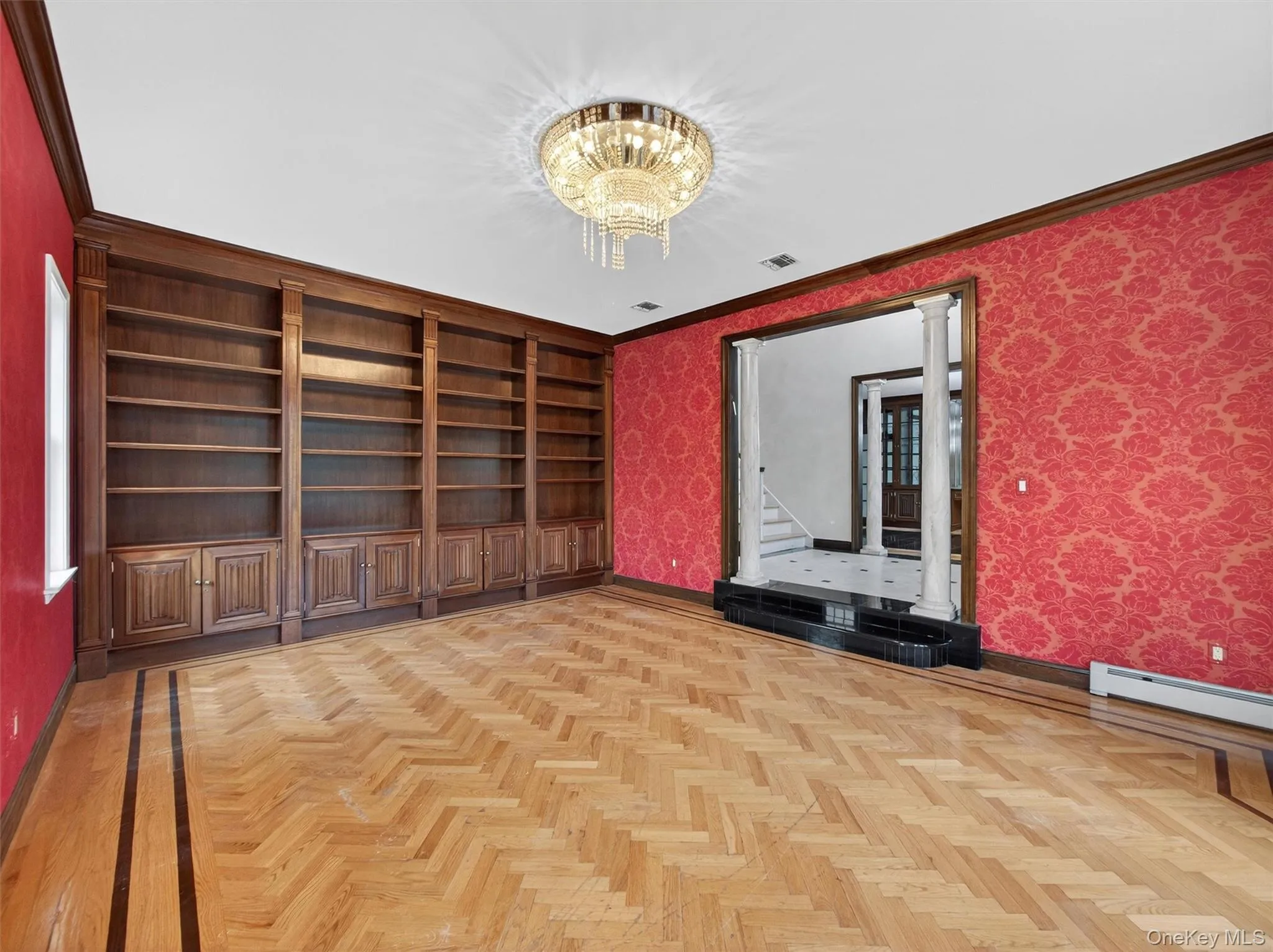 Spare room featuring a chandelier, wallpapered walls, ornamental molding, and built in shelves Spare room featuring a chandelier, wallpapered walls, ornamental molding, and built in shelves