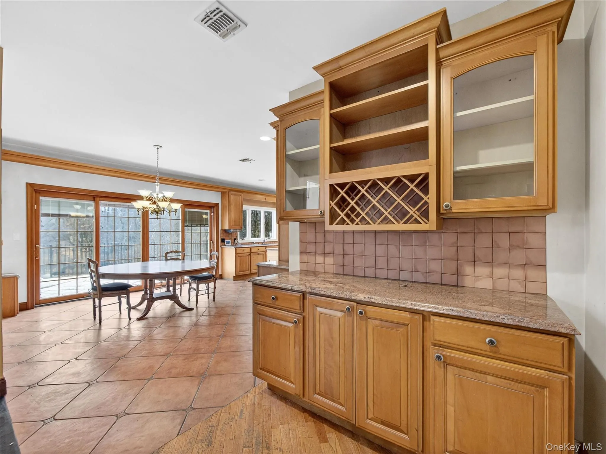 Kitchen with glass insert cabinets, pendant lighting, a chandelier, ornamental molding, and light stone counters Kitchen with glass insert cabinets, pendant lighting, a chandelier, ornamental molding, and light stone counters