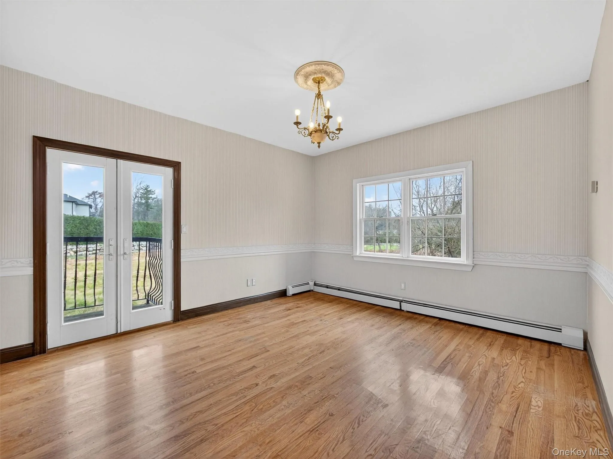 Empty room featuring wallpapered walls, light wood-type flooring, baseboard heating, french doors, and a chandelier Empty room featuring wallpapered walls, light wood-type flooring, baseboard heating, french doors, and a chandelier