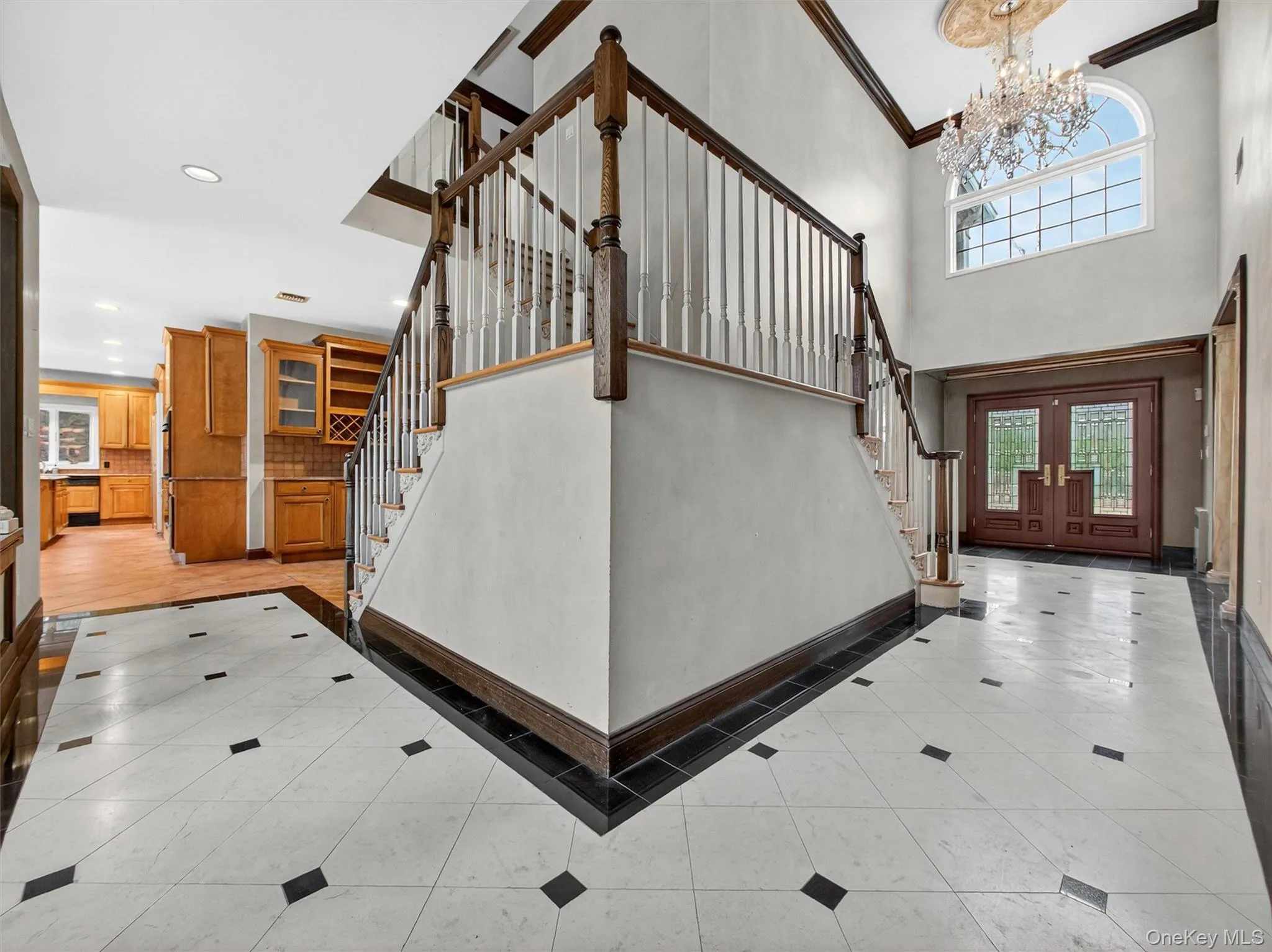 Entryway featuring stairs, light tile patterned floors, a chandelier, ornamental molding, and inlaid floor details Entryway featuring stairs, light tile patterned floors, a chandelier, ornamental molding, and inlaid floor details