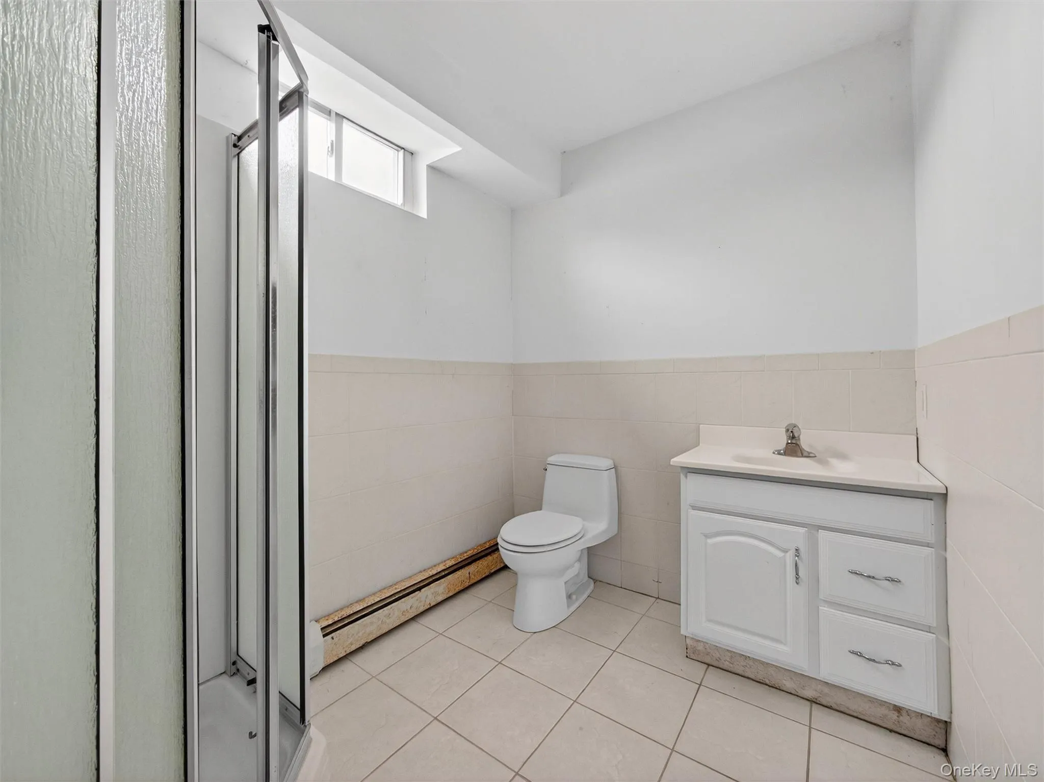 Bathroom featuring tile walls, wainscoting, baseboard heating, vanity, and a stall shower Bathroom featuring tile walls, wainscoting, baseboard heating, vanity, and a stall shower