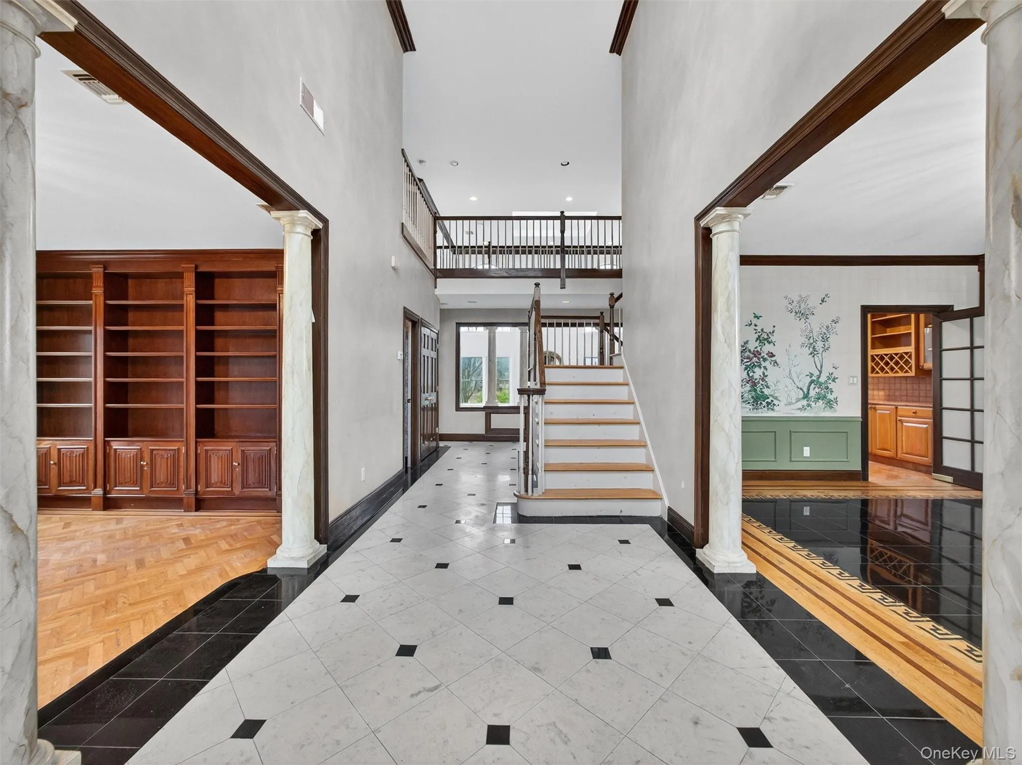 Tiled entryway featuring decorative columns, a towering ceiling, inlaid floor details, stairway, and a wainscoted wall Tiled entryway featuring decorative columns, a towering ceiling, inlaid floor details, stairway, and a wainscoted wall